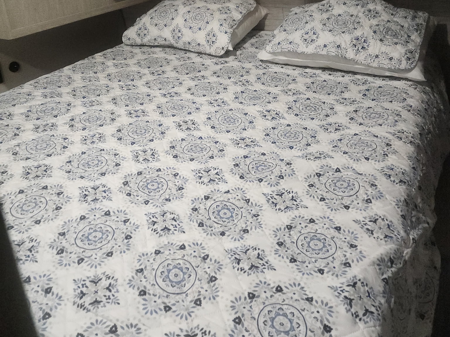Cozy RV rental bedroom with a white and blue patterned comforter and pillows, framed by light wood cabinets above.. Coachmen 29THS 2025