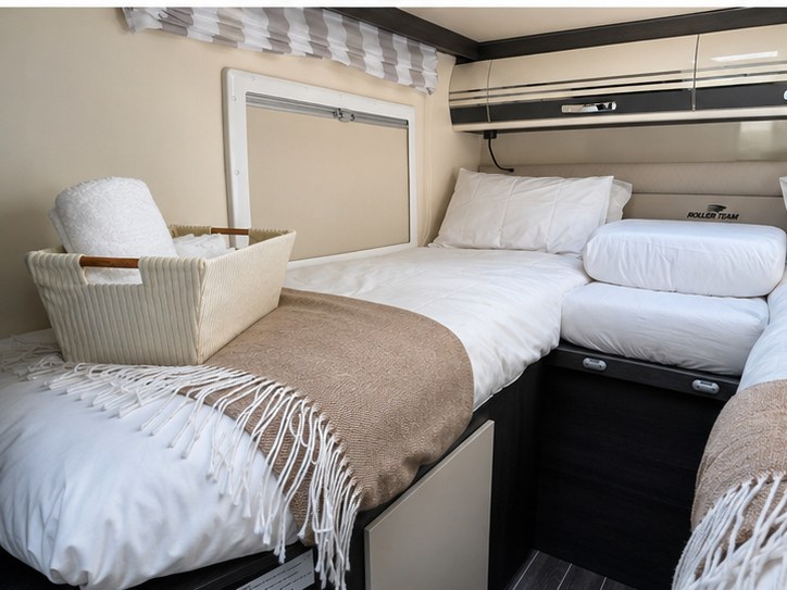 Comfortable RV rental sleeping area featuring two single beds with white bedding, throw blankets, and overhead storage for a cozy camper trip.. FORD TRANSIT 2026