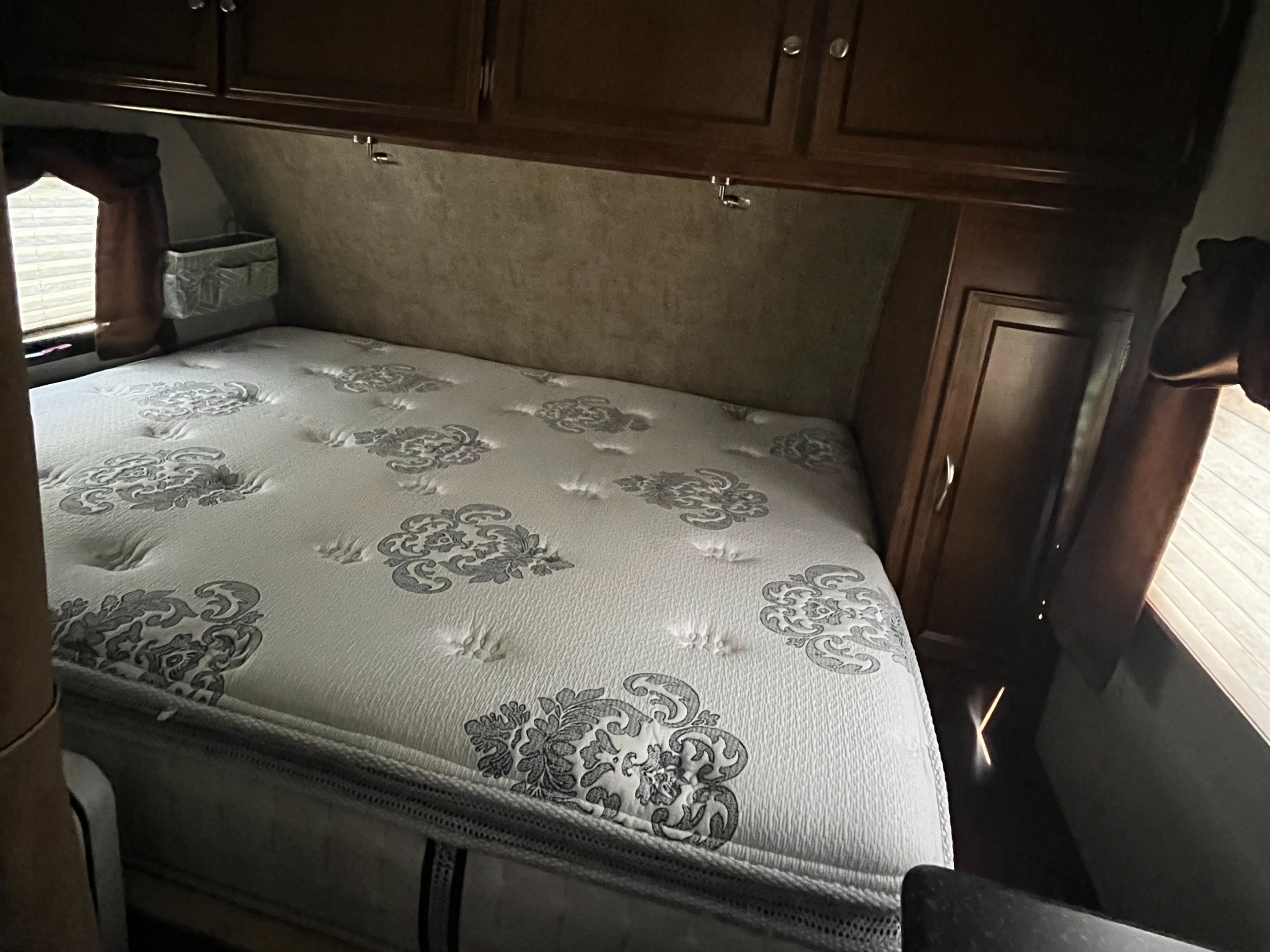 RV rental bedroom with patterned mattress, overhead storage cabinets, and side window, offering a compact, comfortable space.. Coachmen Freedom Express 2017