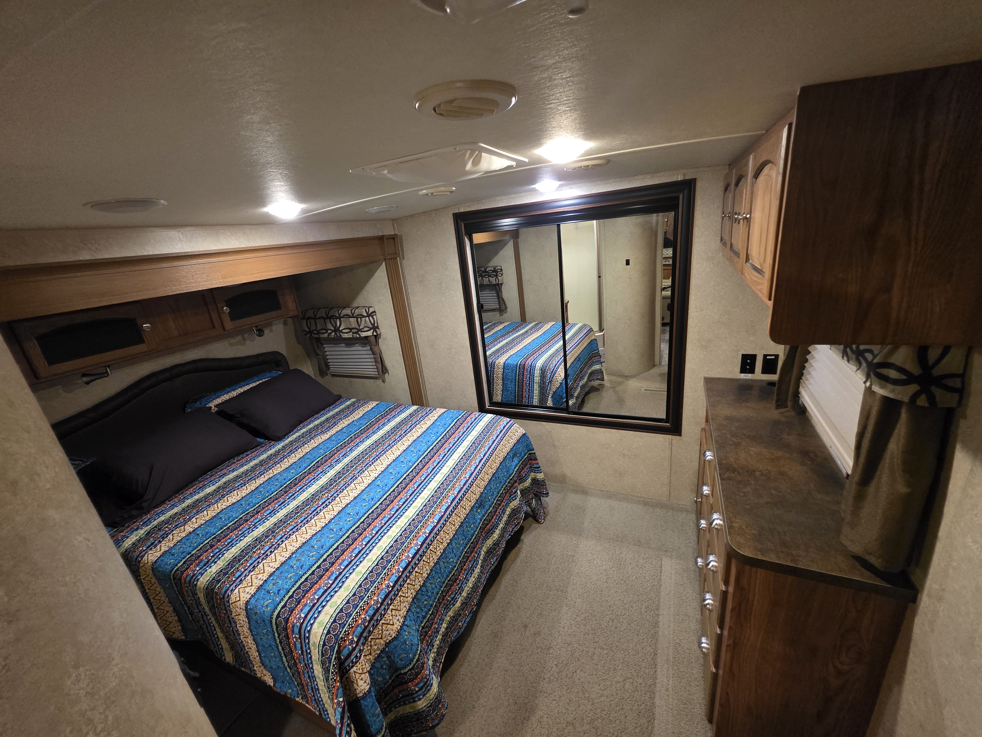 Spacious RV rental bedroom featuring a vibrant bedspread, storage, and a mirrored wardrobe. Perfect for road trips!. Forest River Flagstaff Classic Super Lite 2016