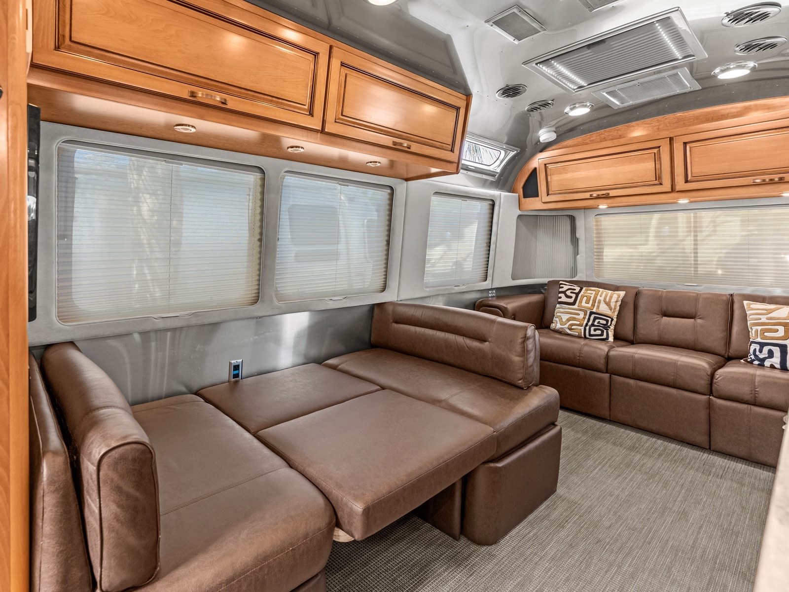 Spacious RV rental interior with brown leather seating, convertible bed, wood cabinets, and large windows.. Airstream Classic 2019