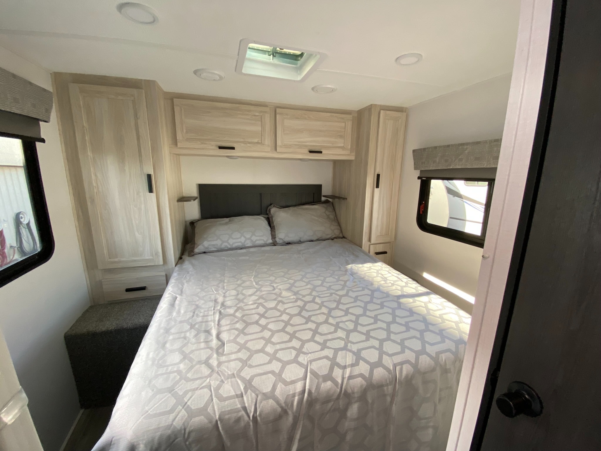 Explore this RV rental's cozy bedroom, featuring a comfortable bed with patterned bedding, overhead cabinets, and windows.. Forest River Sunseeker LE 2023