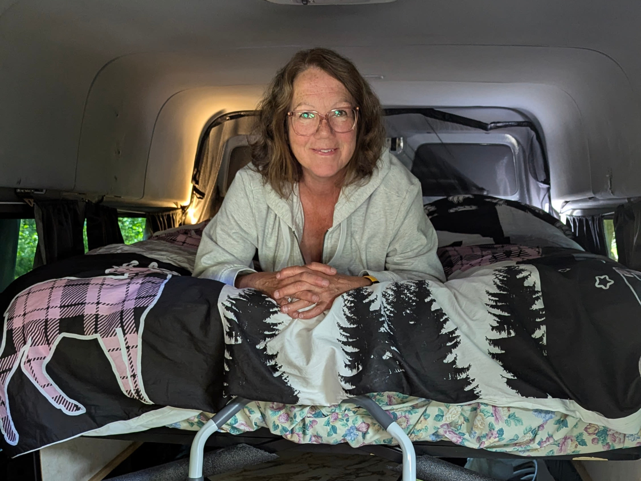 Smiling woman on a loft bed in her camper van, featuring a ladder, toilet, and storage. Ideal for your next RV rental trip!. Mercedes Sprinter 2008