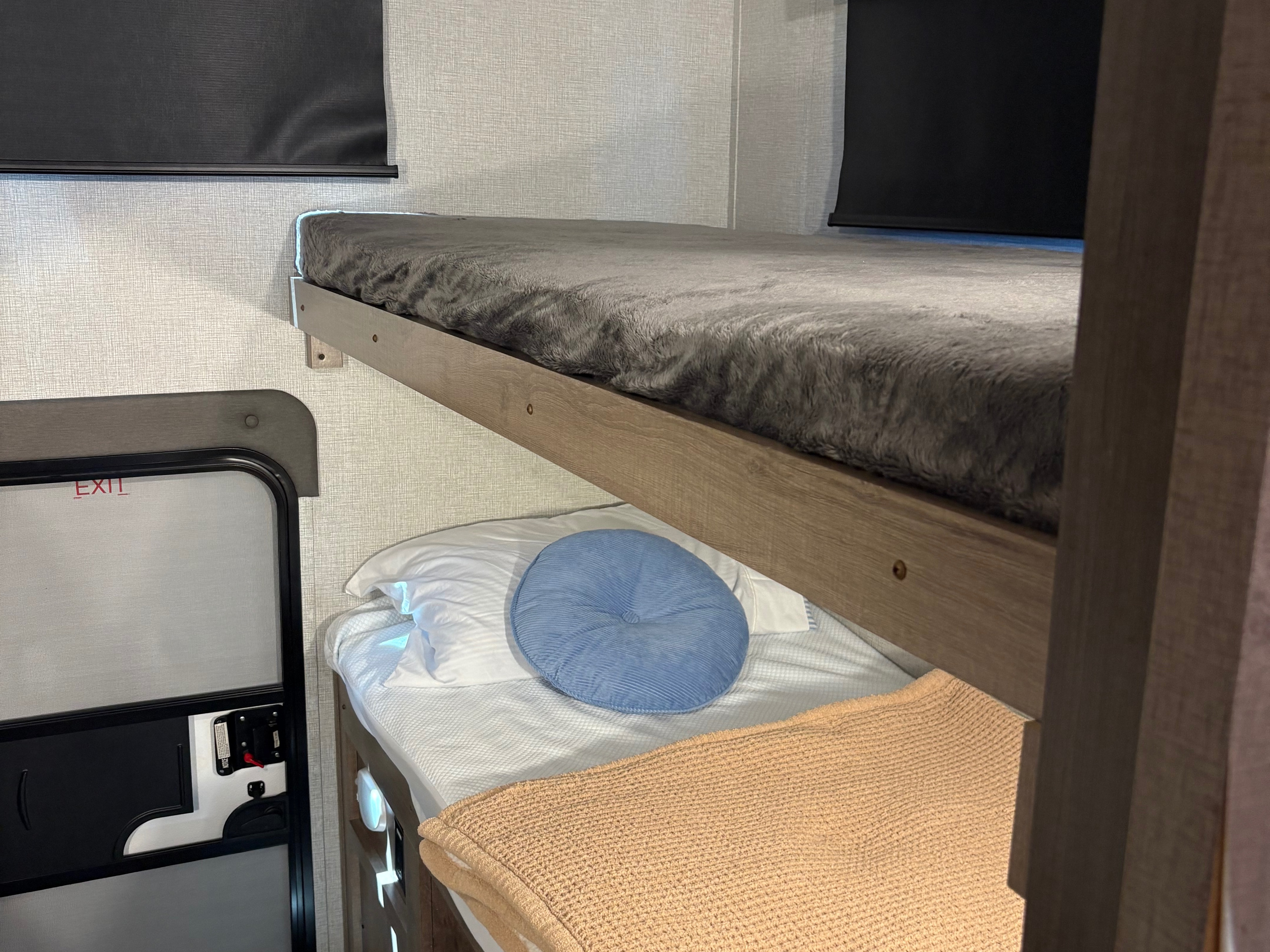 Cozy RV rental bunk beds with soft blankets, pillows, and an exit door nearby.. Grand Design Imagine XLS 2023