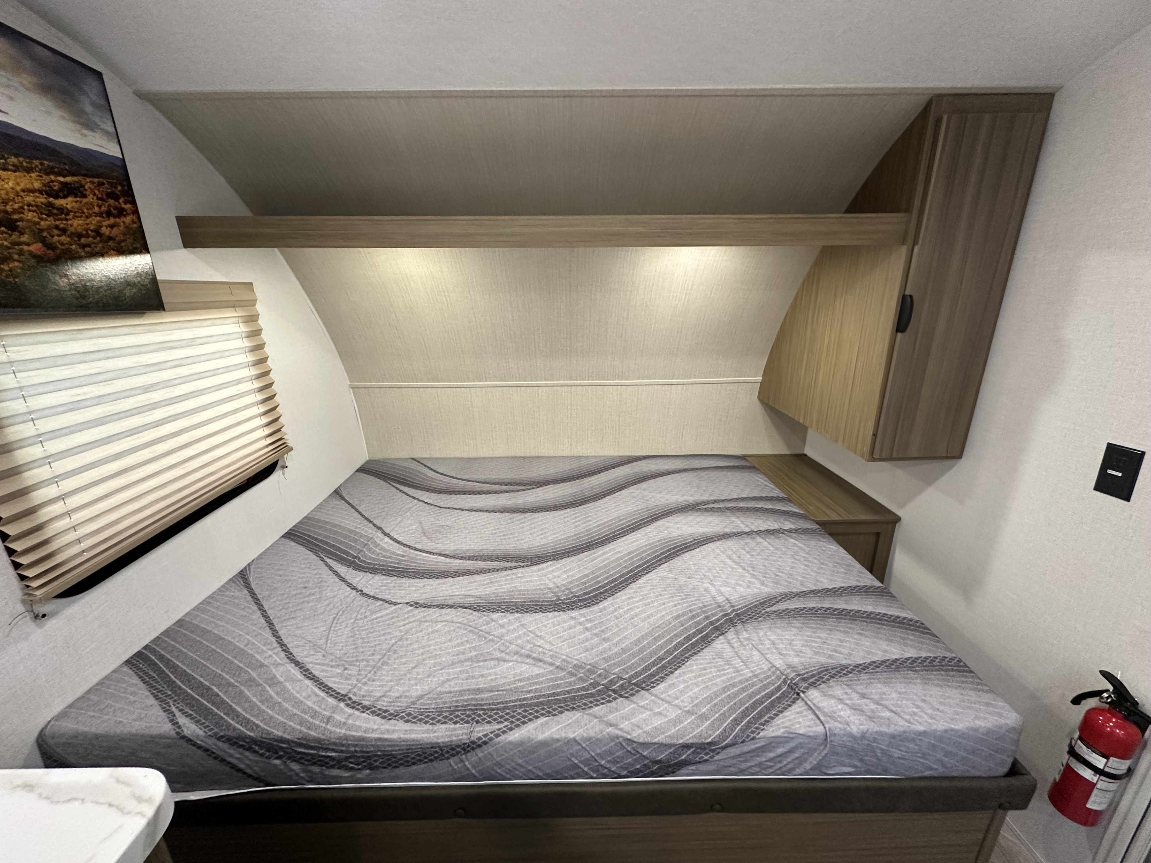 RV rental bedroom: bed with patterned mattress, overhead storage, window blinds, TV, and a fire extinguisher.. Forest River Salem 2026