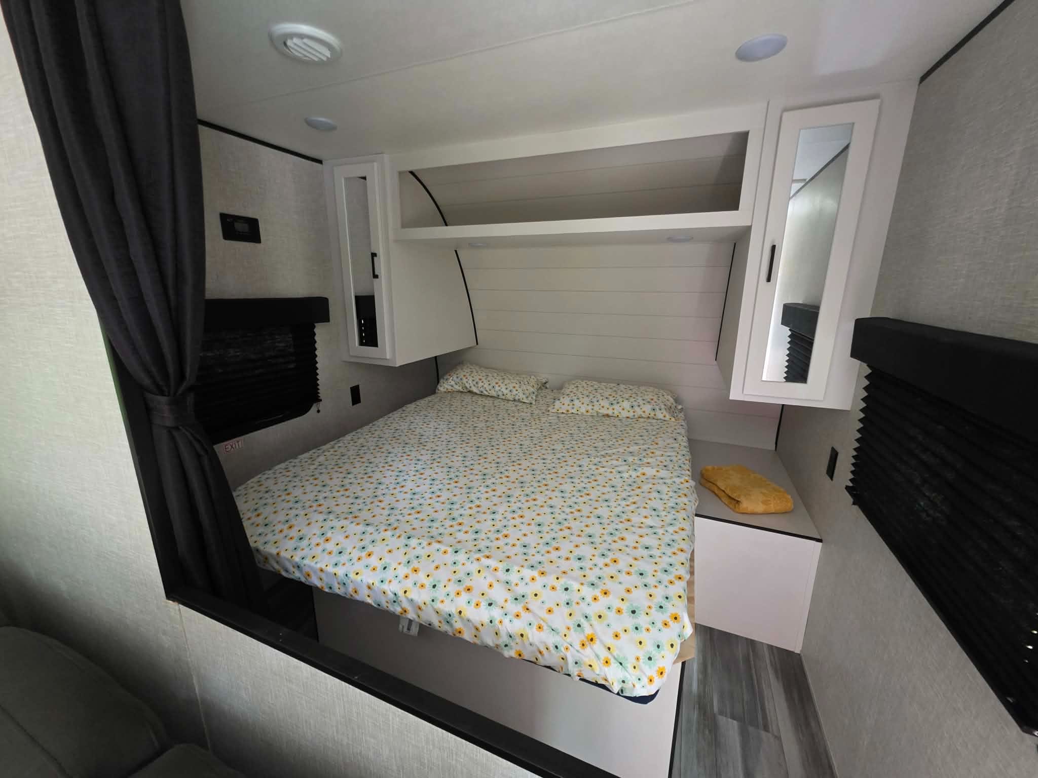 Spacious RV rental bedroom with a comfy bed, floral sheets, overhead cabinets, and a bedside stand with a towel.. Jayco Jay Flight SLX 2024