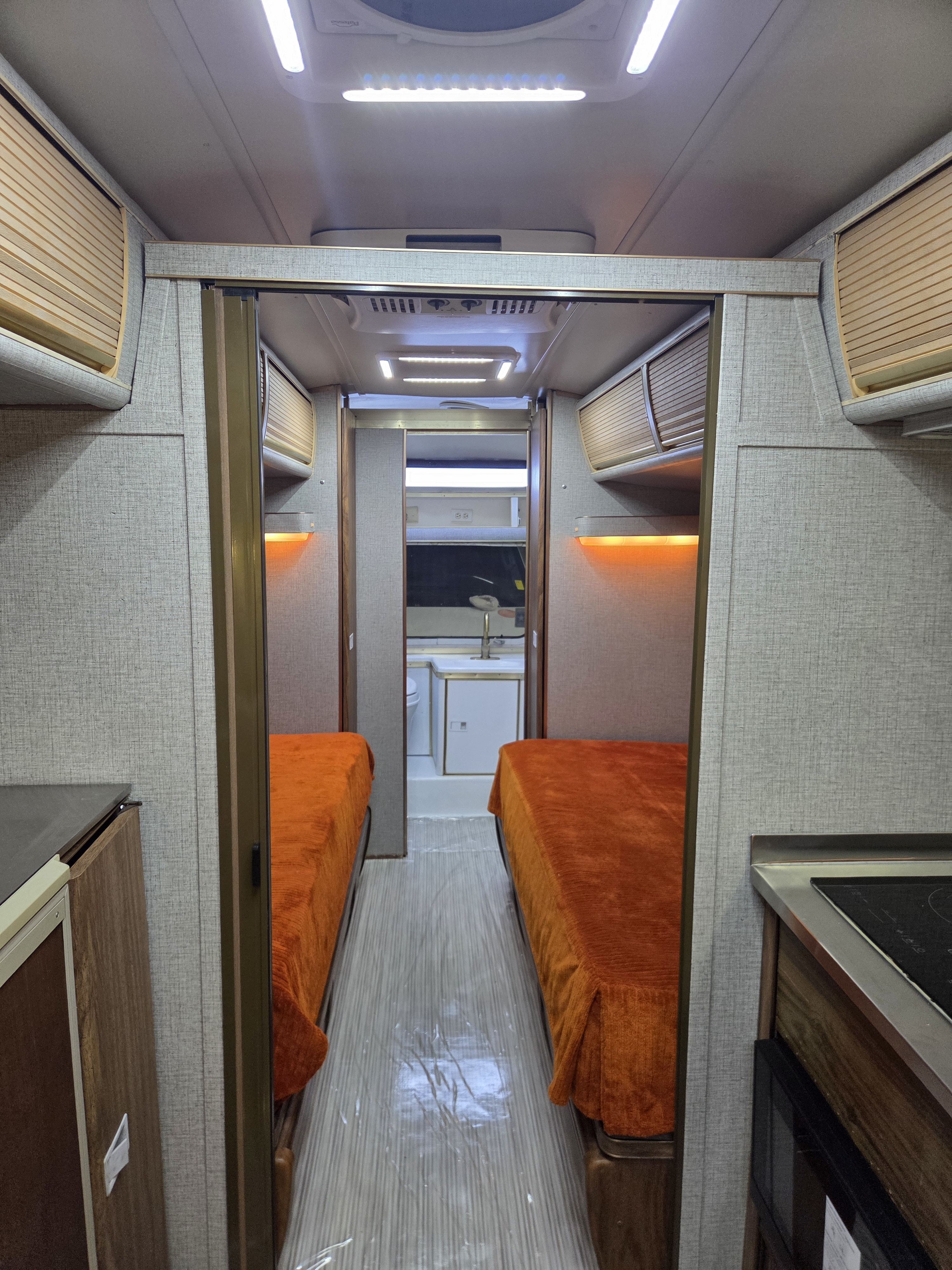 RV rental interior: twin beds with bright orange covers, narrow hallway, compact kitchen, and overhead storage.. Airstream Airstream Trailer 1977