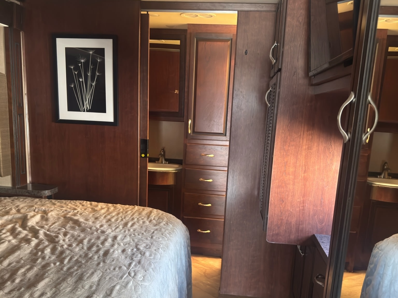 RV rental bedroom with a quilted bed, dark wood walls, and a glimpse of the bathroom sink through the open door.. Fleetwood 35 K 2017