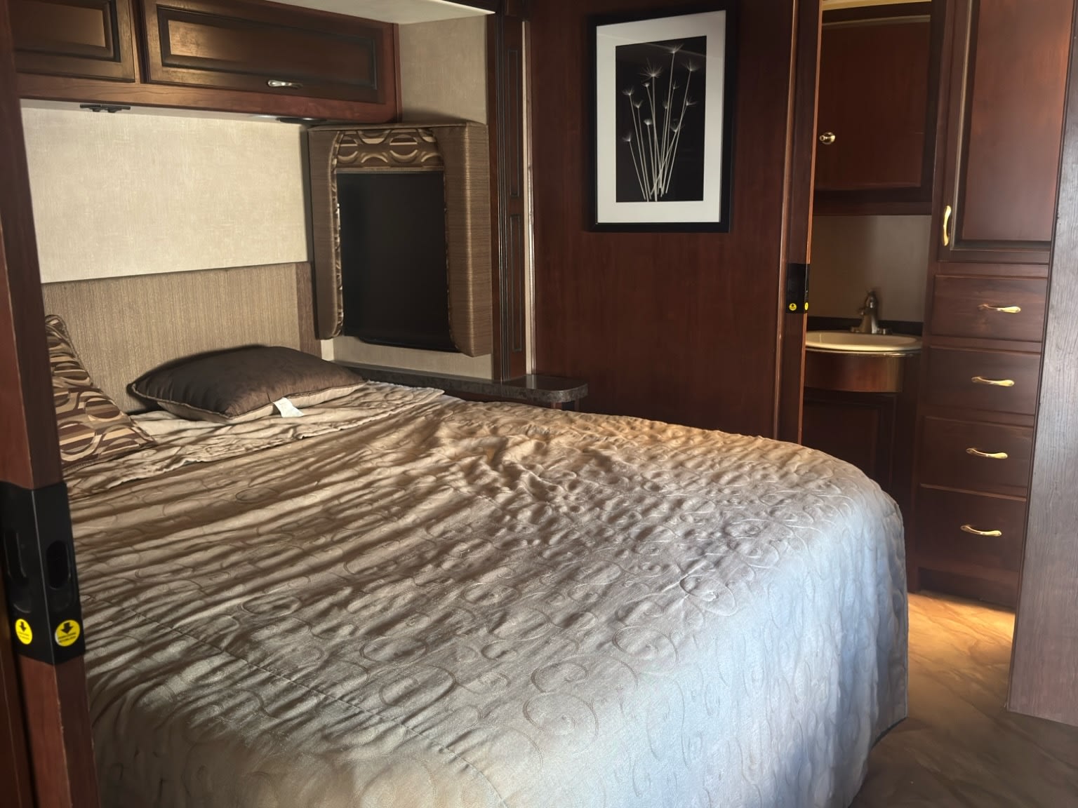 This cozy RV rental features a compact bedroom with a comfortable bed, overhead cabinets, and an adjacent bathroom sink area.. Fleetwood 35 K 2017