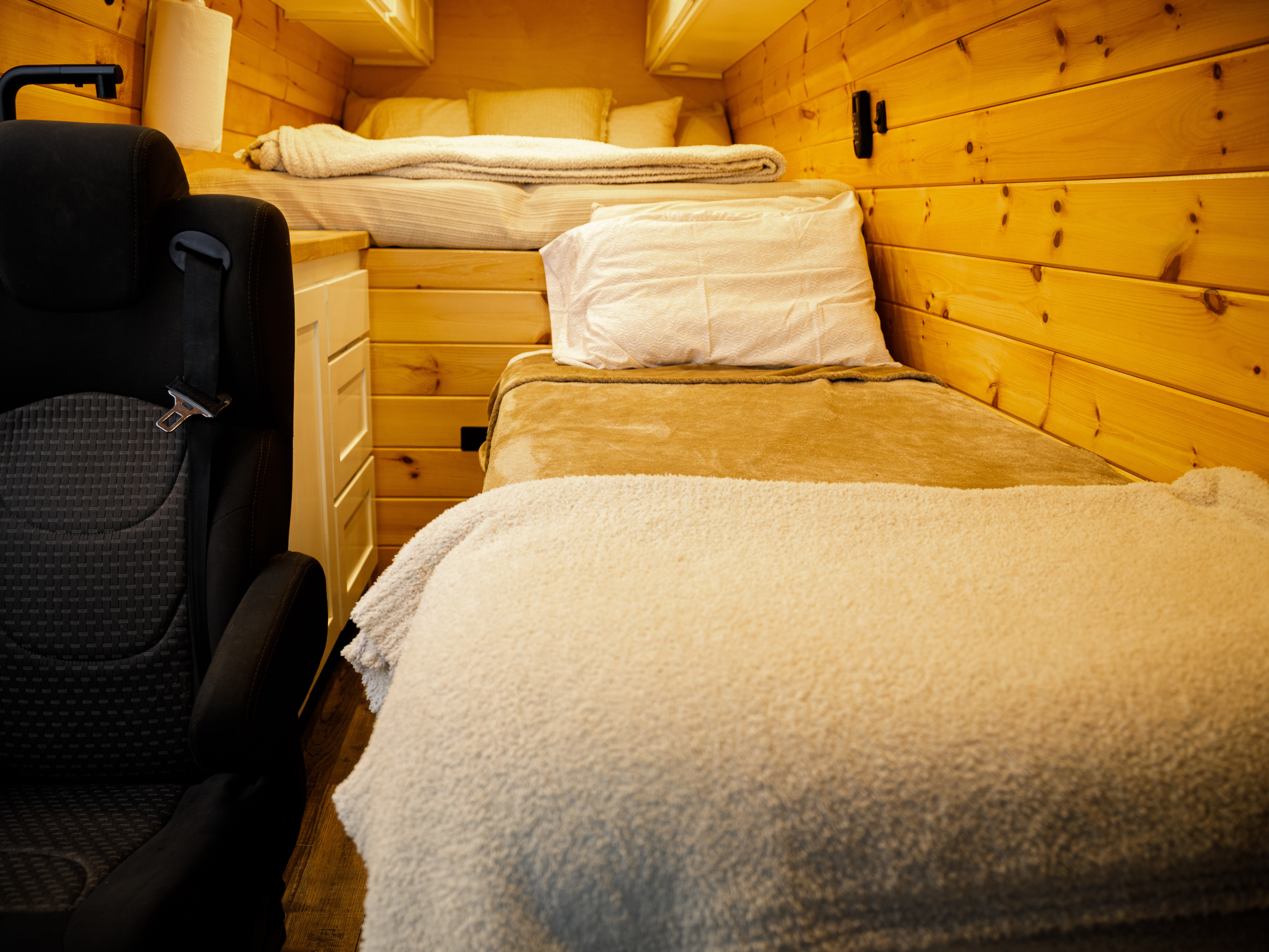 Inside a cozy rv rental, wooden-paneled camper van. Features a lower bed, upper bunk, and a seat with a seatbelt.. Mercedes Benz Sprinter 2017