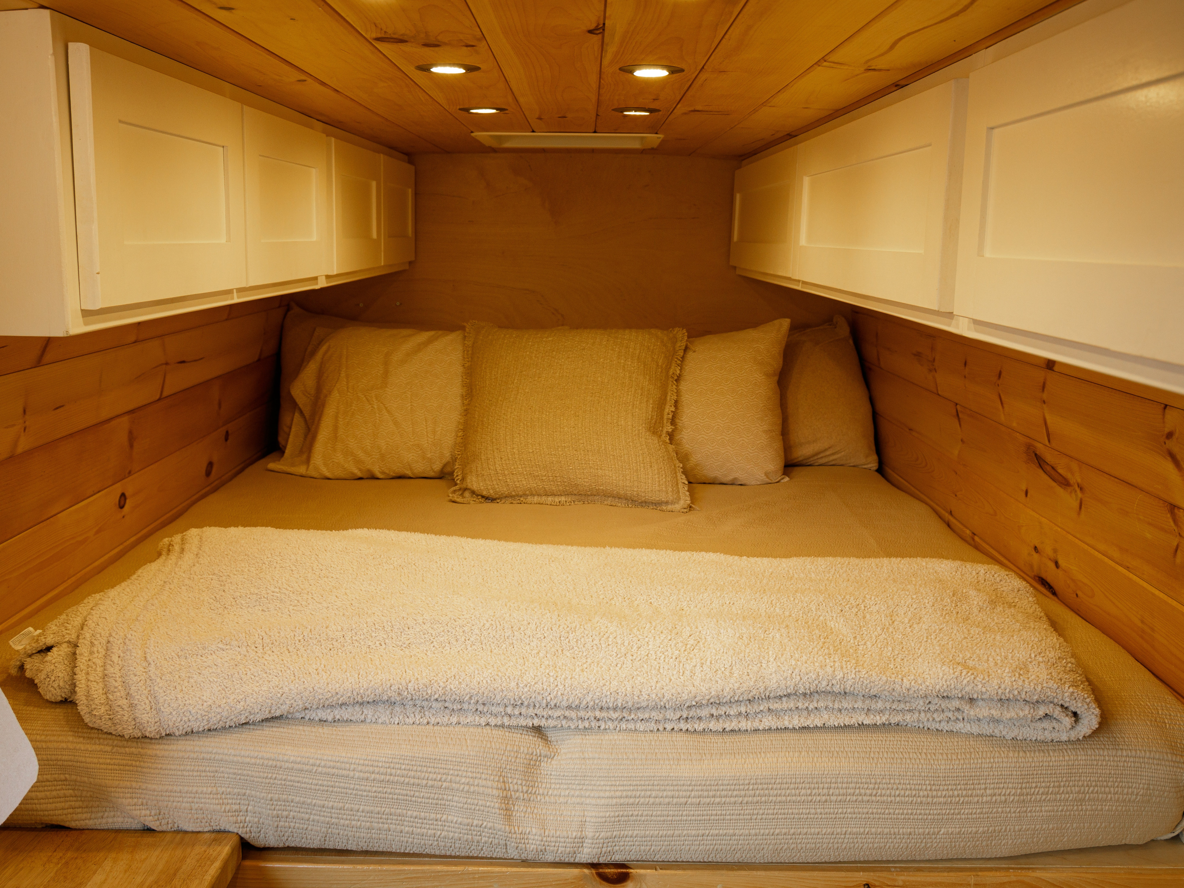 Cozy RV rental interior featuring a comfortable bed with neutral bedding, wood paneling, and white overhead cabinets.. Mercedes Benz Sprinter 2017