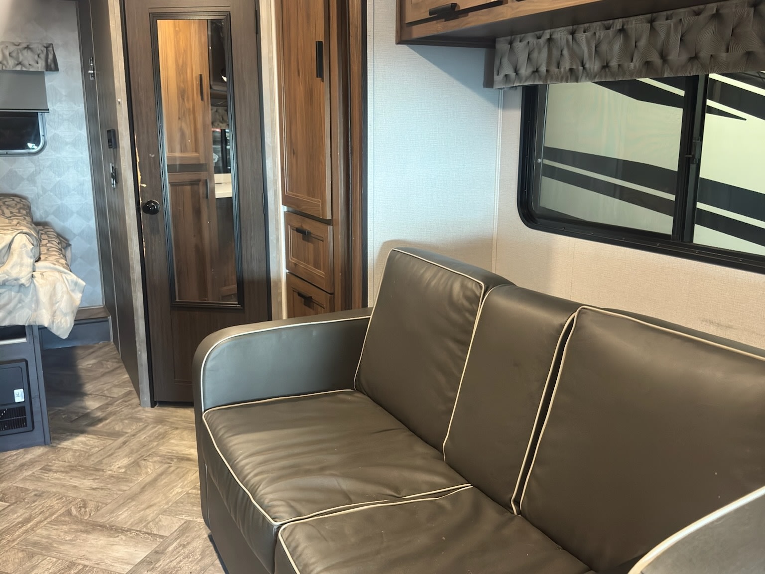 RV rental interior featuring a comfy sofa, bed, mirror door, and stylish wood-look flooring.. Forest River Sunseeker LE 2022