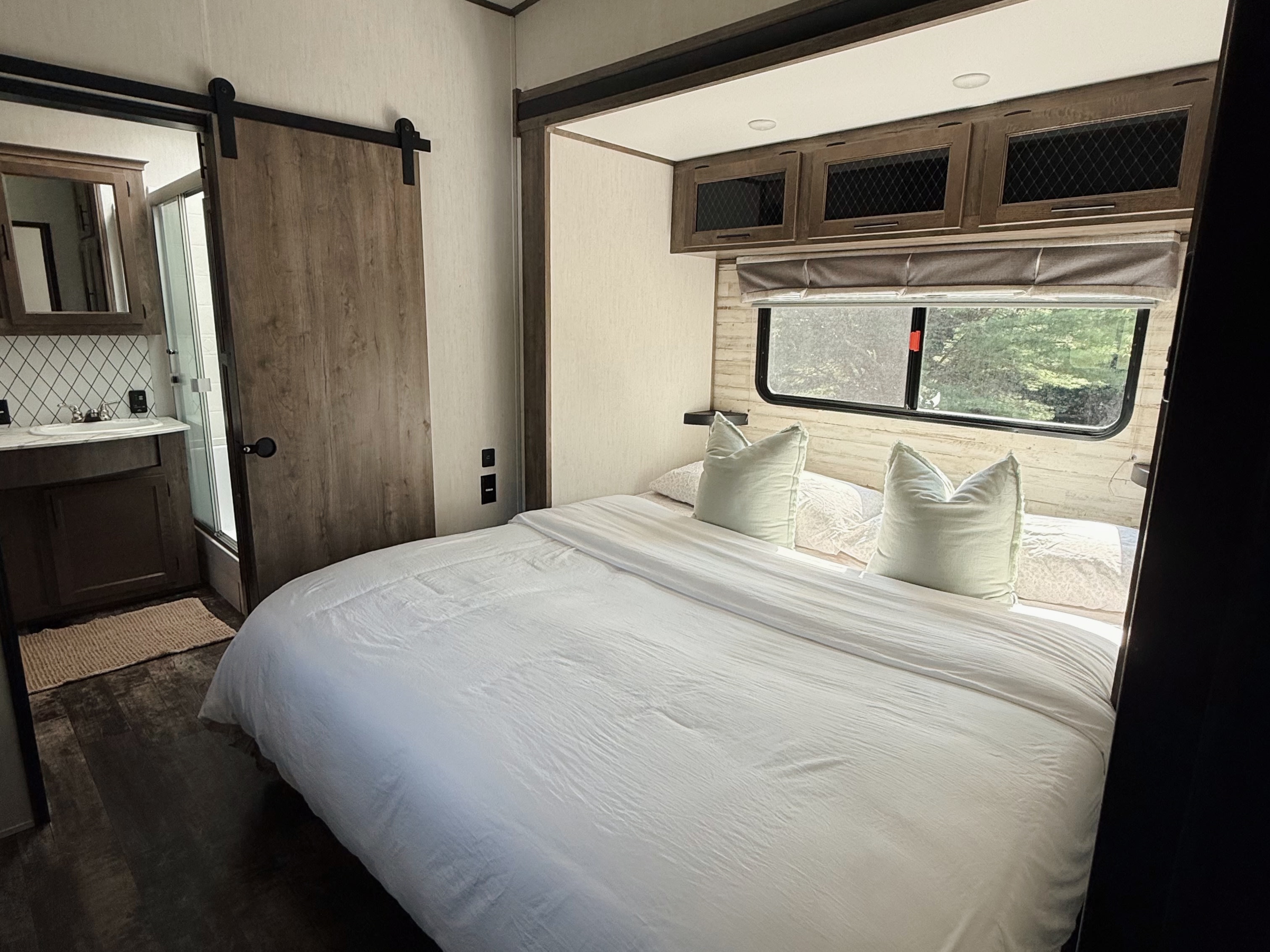 Cozy RV rental bedroom with a comfortable white bed, window views, and a barn door leading to the bathroom.. Forest River Sabre 2021