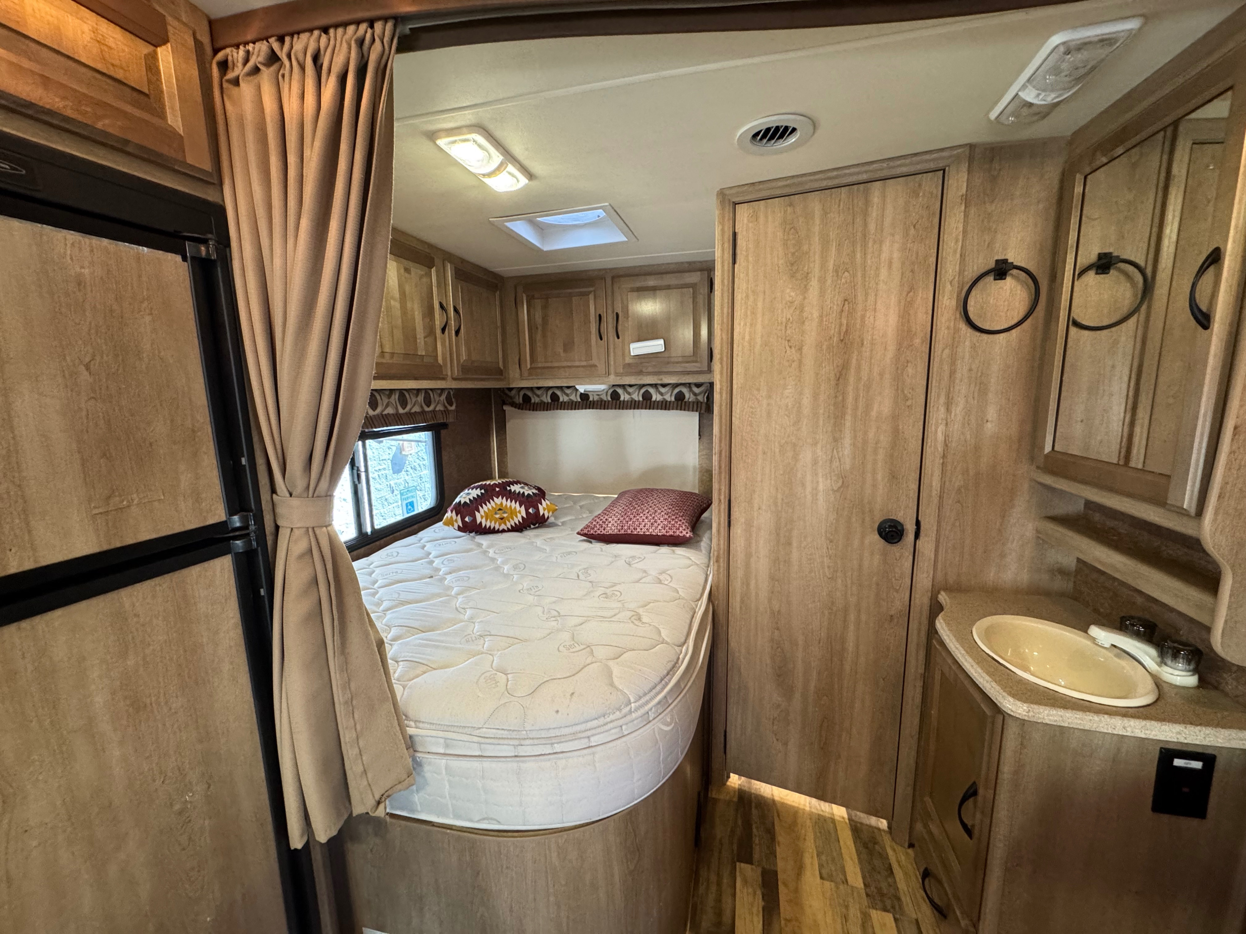RV rental interior: cozy bedroom with bed, window, and curtains. Includes a compact bathroom vanity with a sink.. Forest River Coachmen Prism 2015