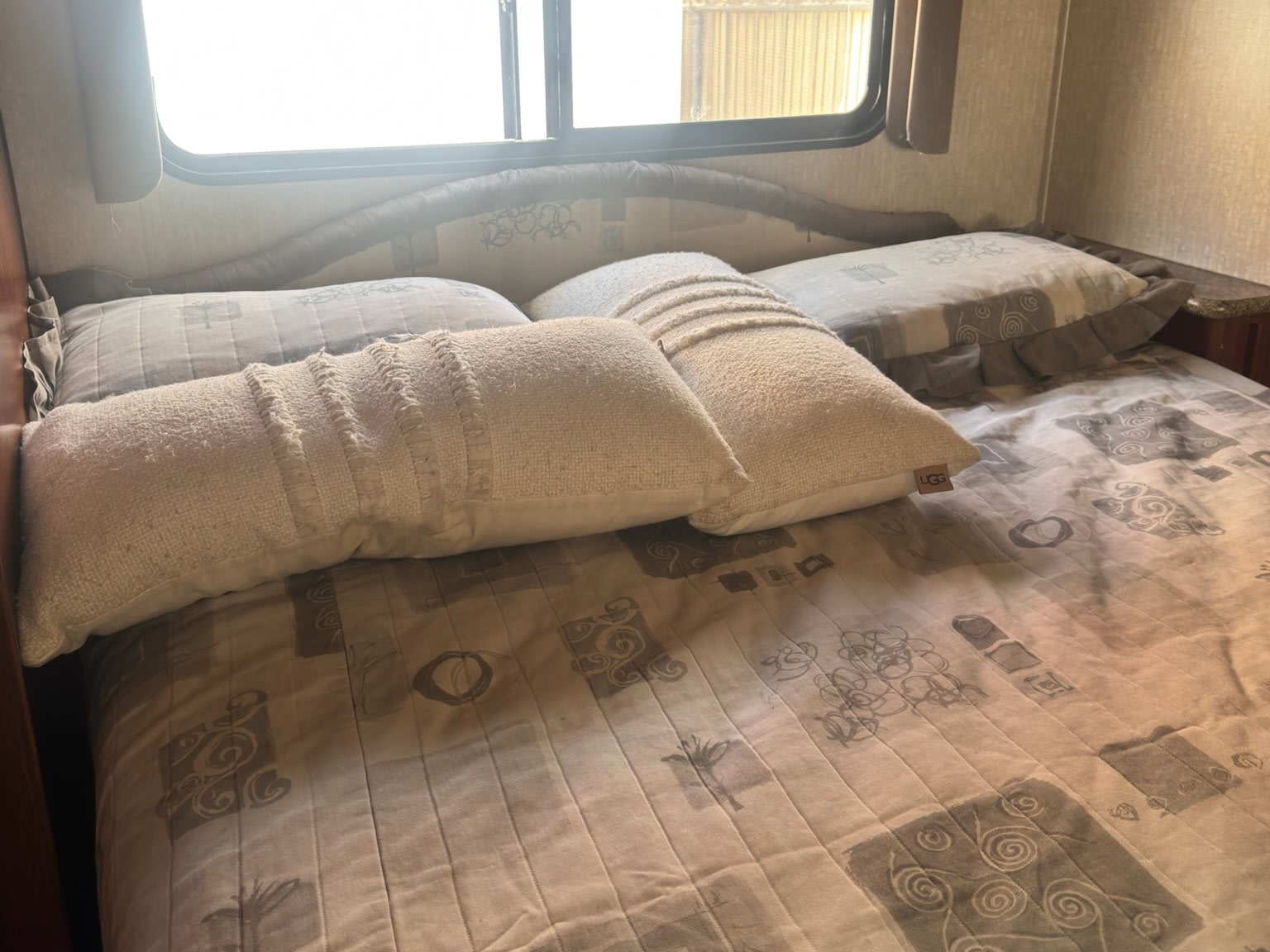 RV rental bedroom features a cozy bed with cream pillows, including one with a "UGG" tag, and a patterned comforter.. Fleetwood Fiesta 2009