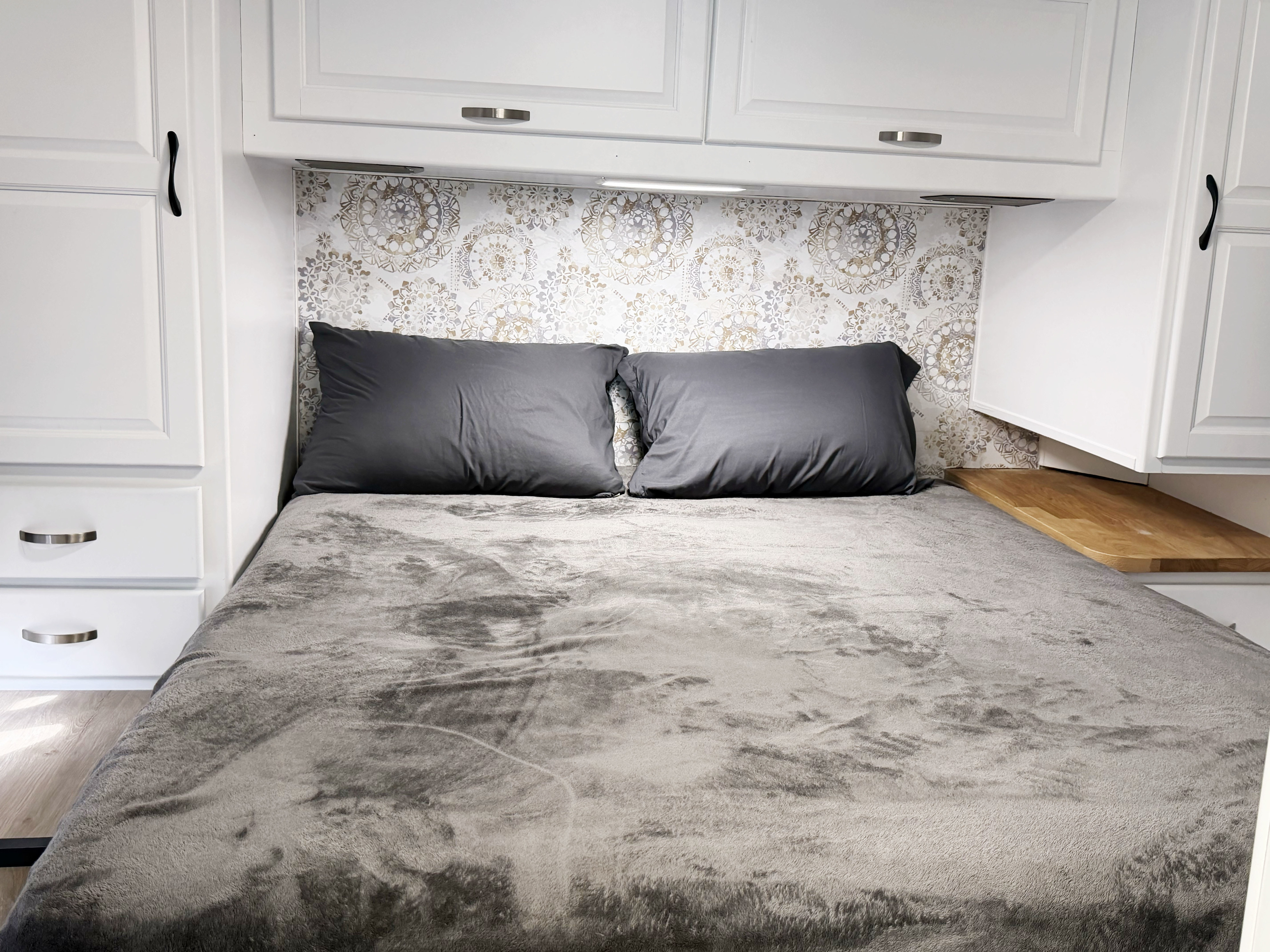 Cozy RV rental bedroom: grey bed, patterned headboard, white cabinets with varied handles, and a wooden nightstand.. Thor Majestic 2014