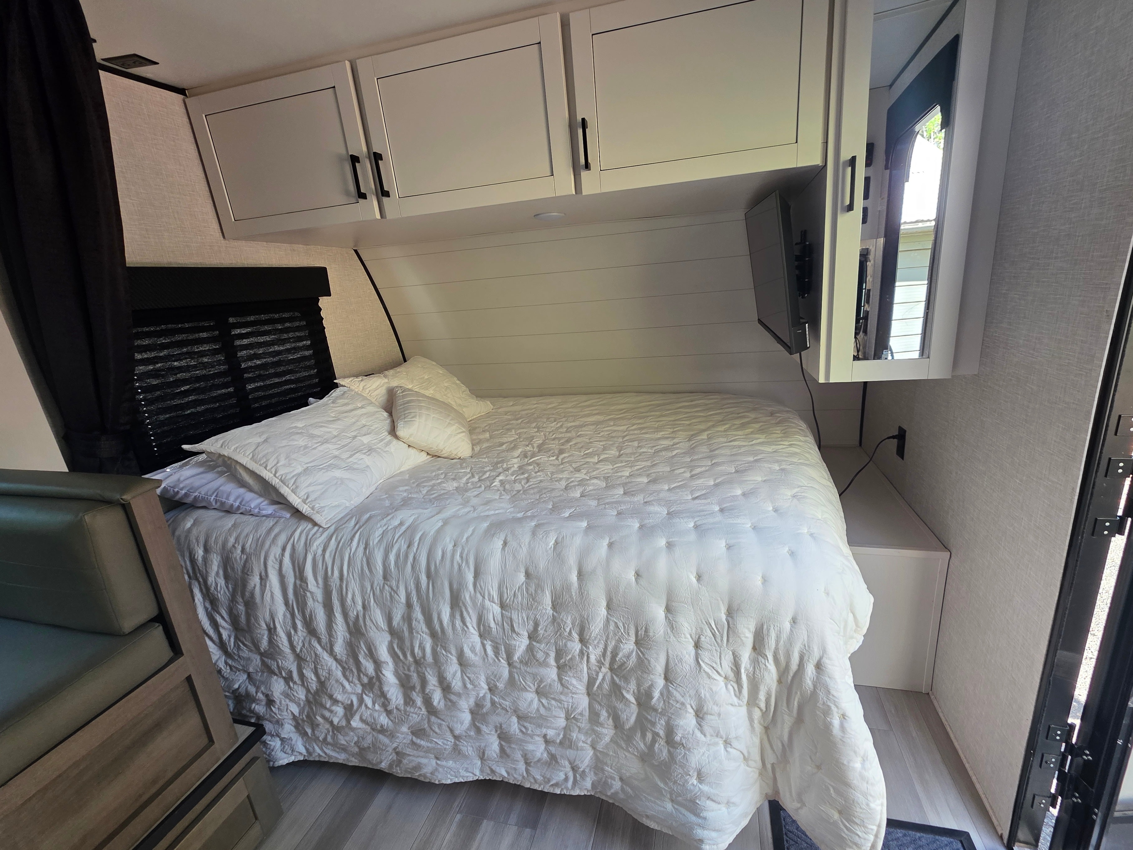 Cozy RV rental bedroom with a large white bed, overhead storage, and a wall-mounted TV, perfect for travel.. Highland Ridge Open Range MOAB 2025