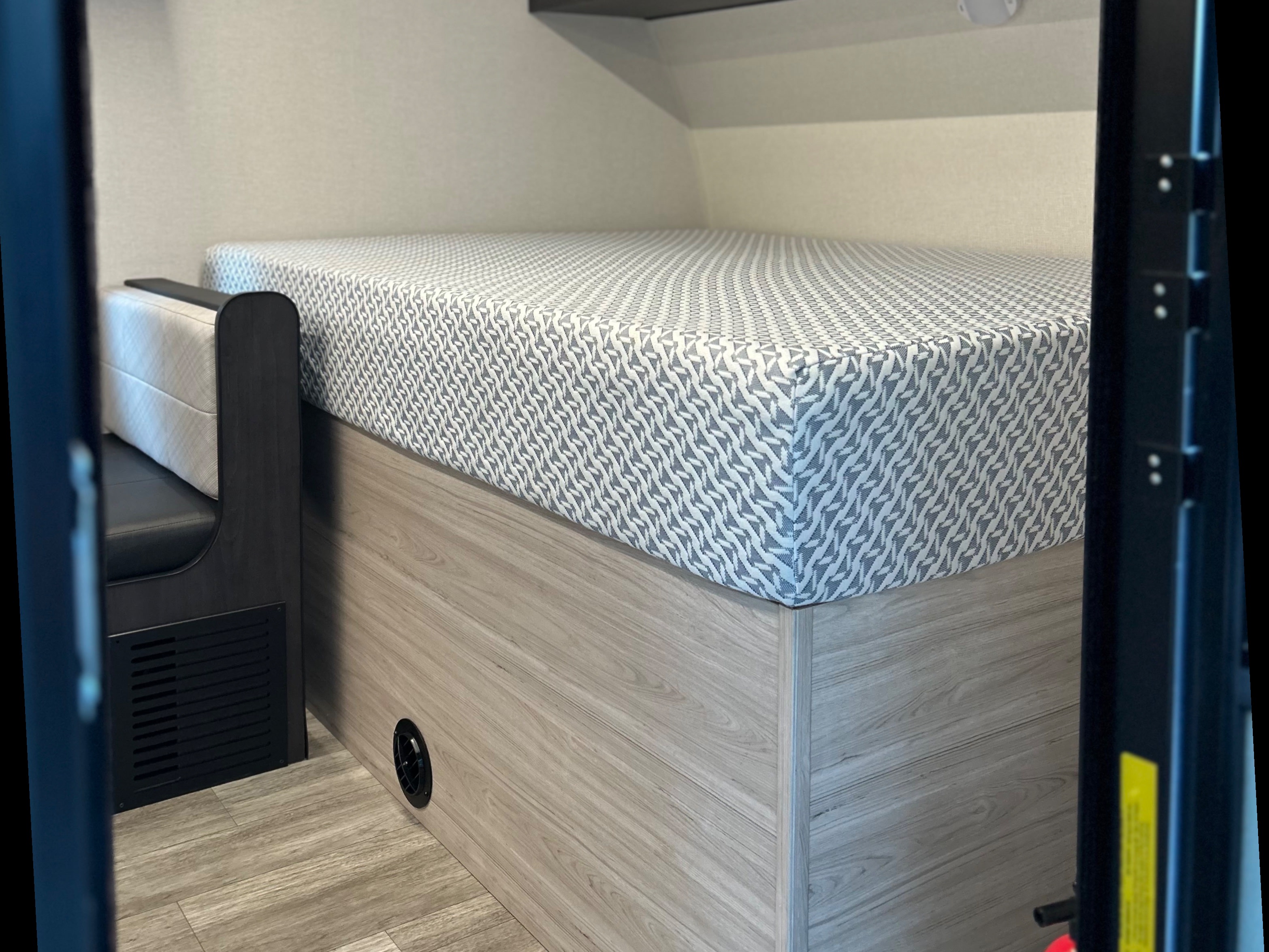 Compact rv rental interior with a bed featuring a patterned mattress on a wood-look base and an adjacent dinette.. Heartland RVs Mallard 2025