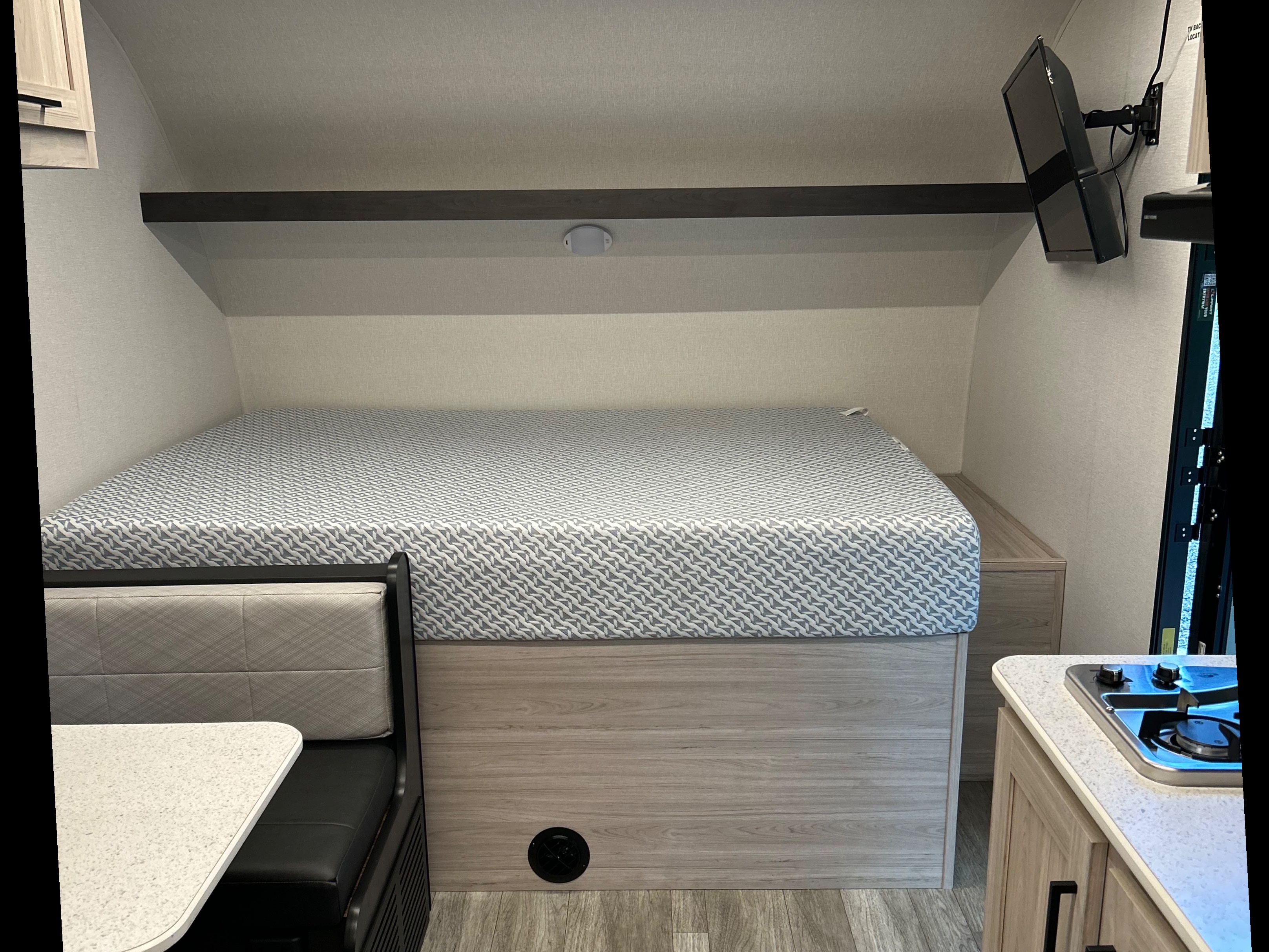 Inside this RV rental: a compact sleeping area with a patterned mattress, alongside a dining booth and stovetop.. Heartland RVs Mallard 2025