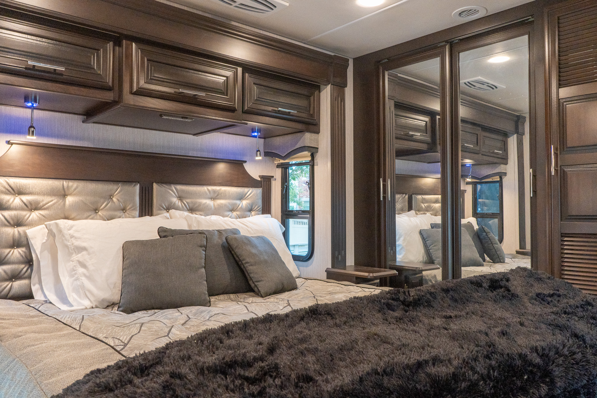 This luxurious RV rental bedroom showcases dark wood cabinetry, a tufted headboard, and mirrored closets, creating a spacious feel.. Berkshire XL 2021