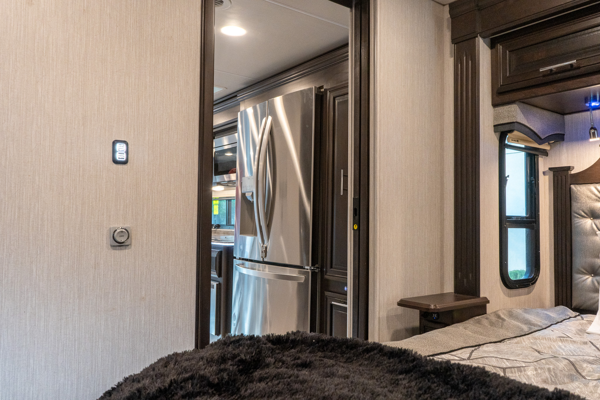 This modern RV rental interior features a comfortable bedroom with a plush bed and controls, adjacent to a kitchen with a stainless steel fridge.. Berkshire XL 2021