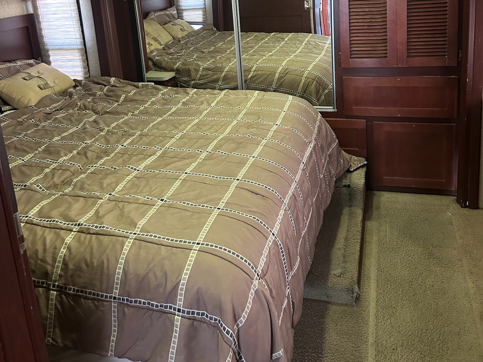 Inside an RV rental, a comfy bedroom features a brown-patterned bed, mirrored closet, and carpeted floor with a step.. Forest River Berkshire 2011