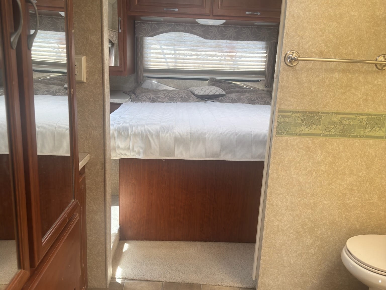 Inside an RV rental: a cozy bedroom with white bedding and wooden cabinets, with a partial view of the adjacent compact bathroom.. Thor Thor Hurricane 2008