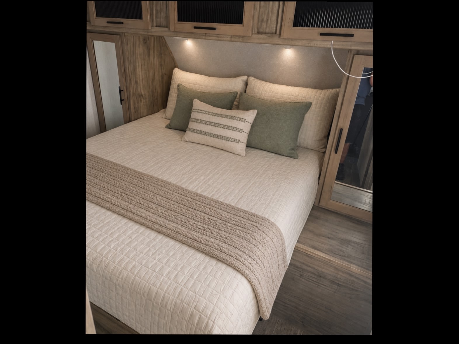 Cozy RV rental bedroom features a comfortable bed with neutral bedding, green pillows, and clever built-in storage for a relaxing stay.. Forest River Cherokee Alpha Wolf 2021