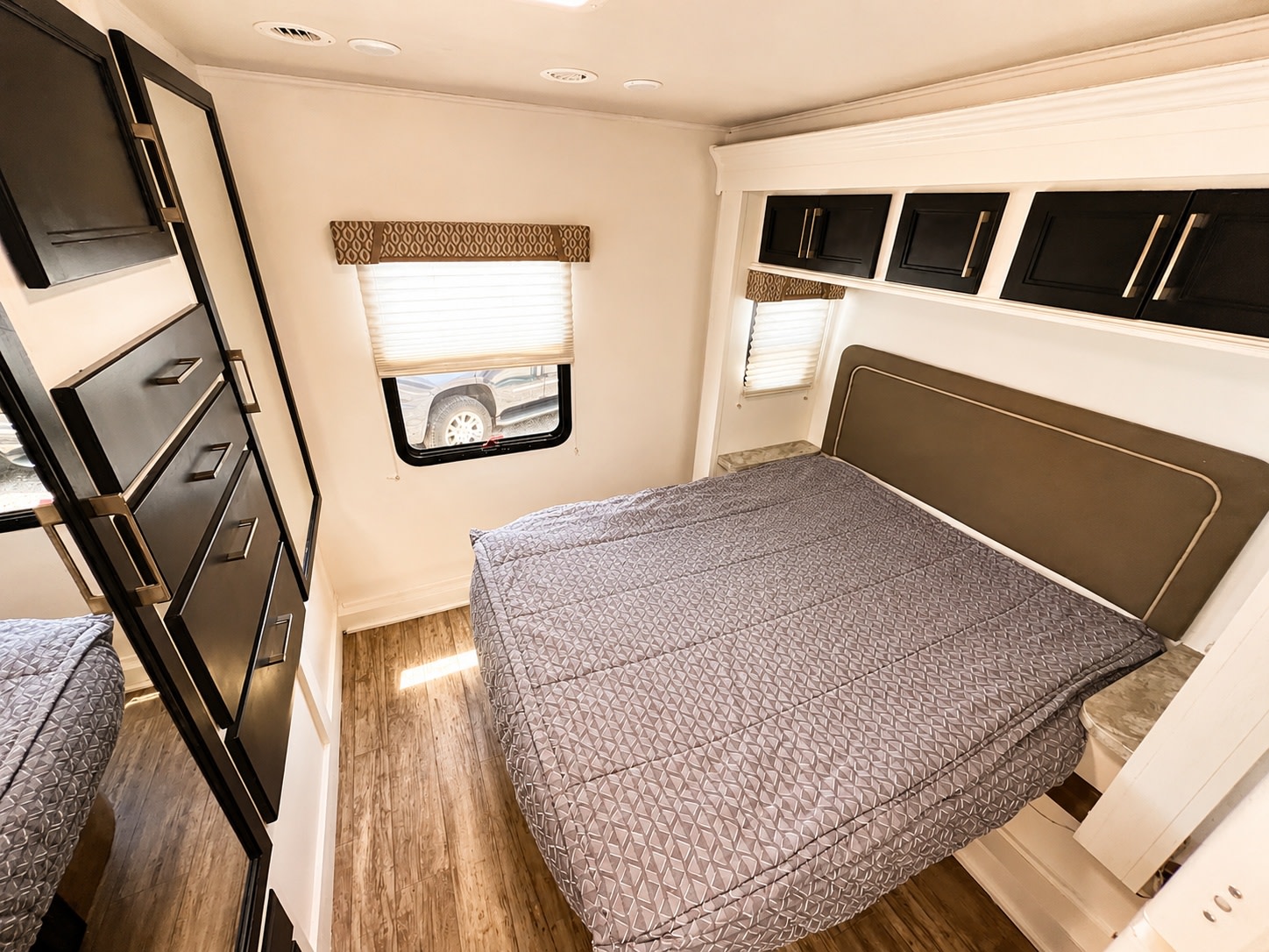 Cozy RV rental bedroom featuring a queen bed, overhead storage, side cabinets, and natural light from compact windows.. Entegra Coach Odyssey 2018