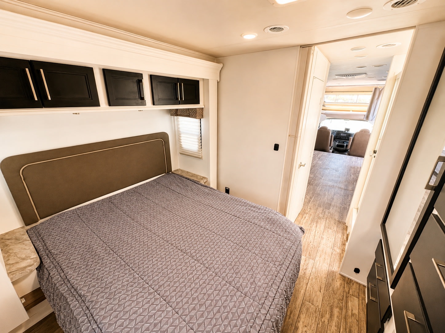 Spacious RV rental bedroom featuring a comfortable bed, overhead storage, and a clear view to the front cockpit area.. Entegra Coach Odyssey 2018