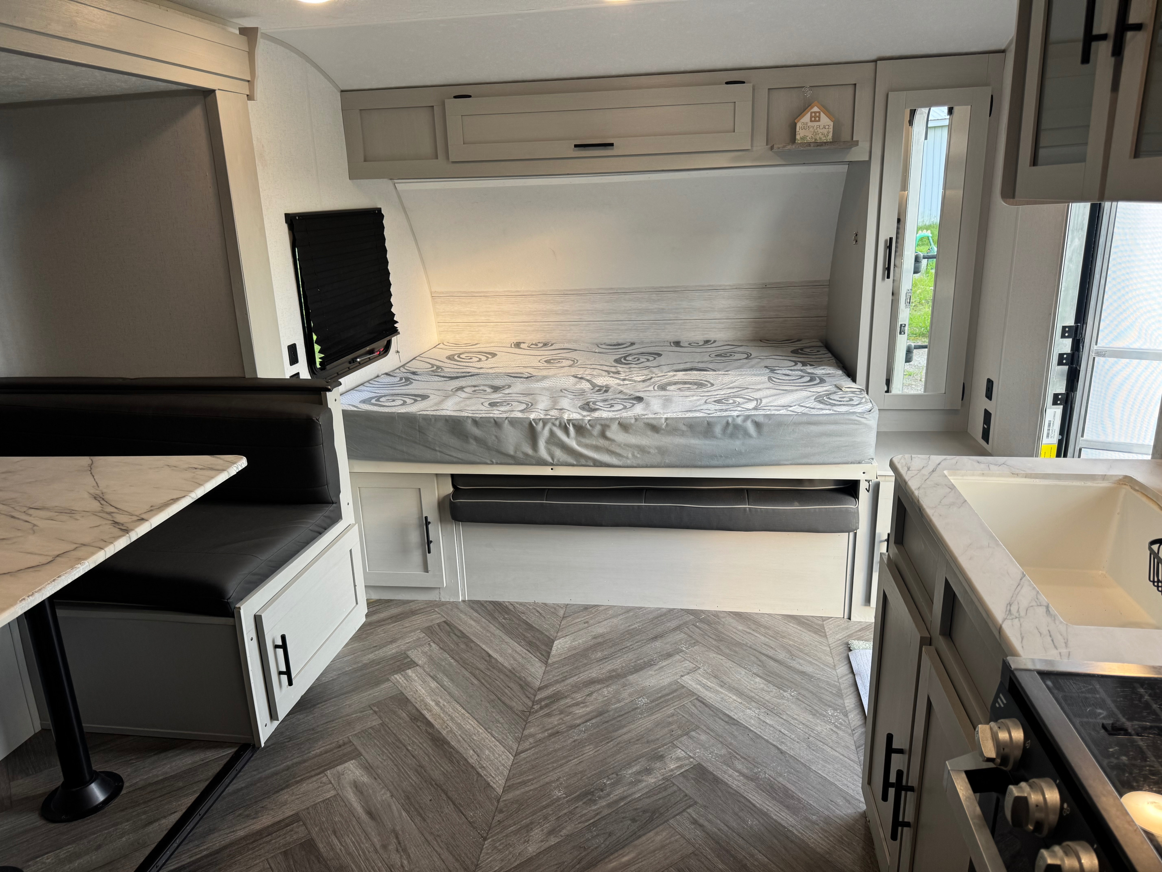 Modern RV rental interior featuring a cozy bed, dinette, and kitchen corner, showcasing light wood finishes and herringbone flooring.. Forest River Wildwood FSX Toy Hauler 2021