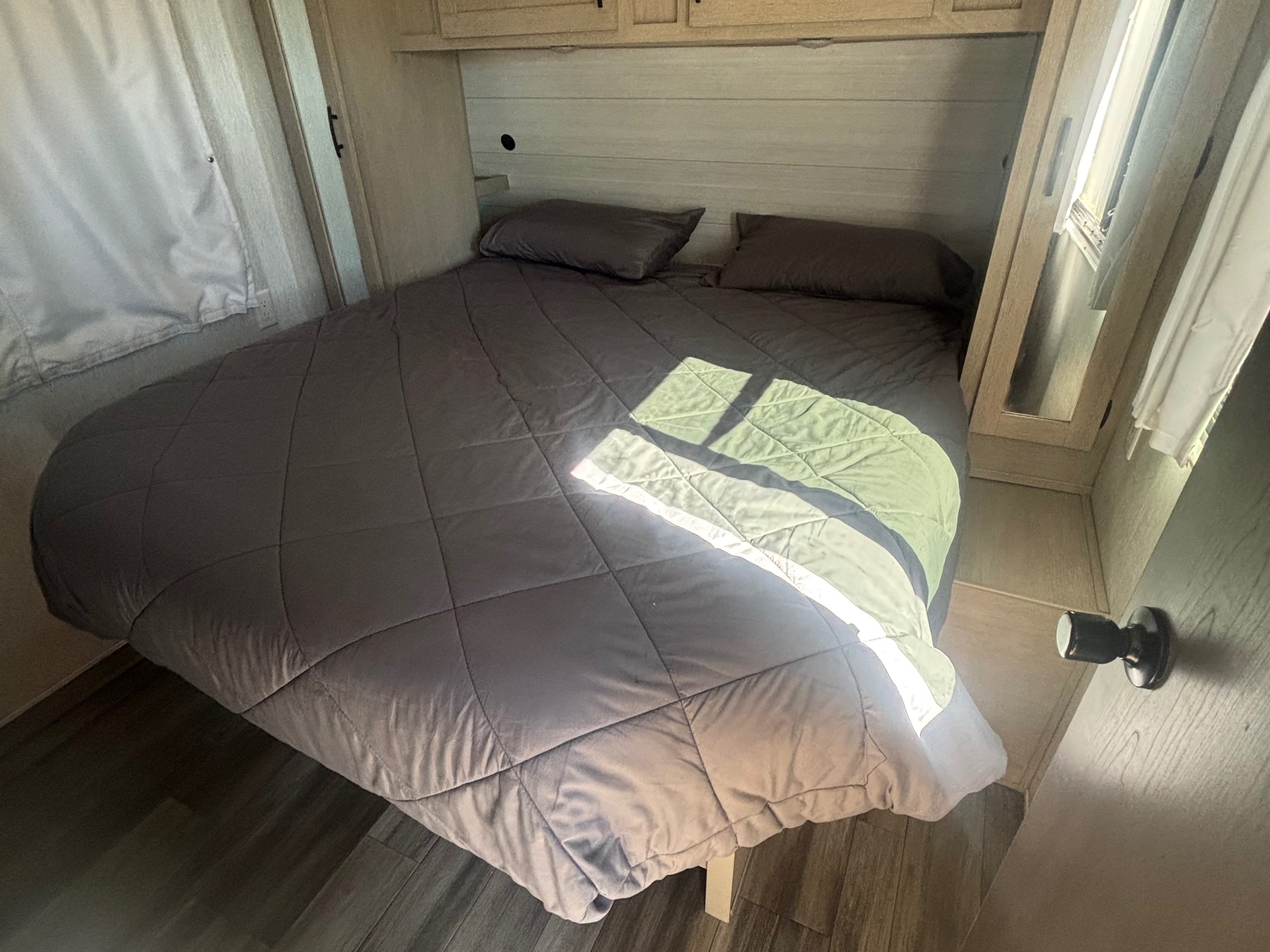 An inviting RV rental bedroom with a gray comforter, light wood interior, and sunlight highlighting the comfy bed.. Forest River Evo 3005 2024
