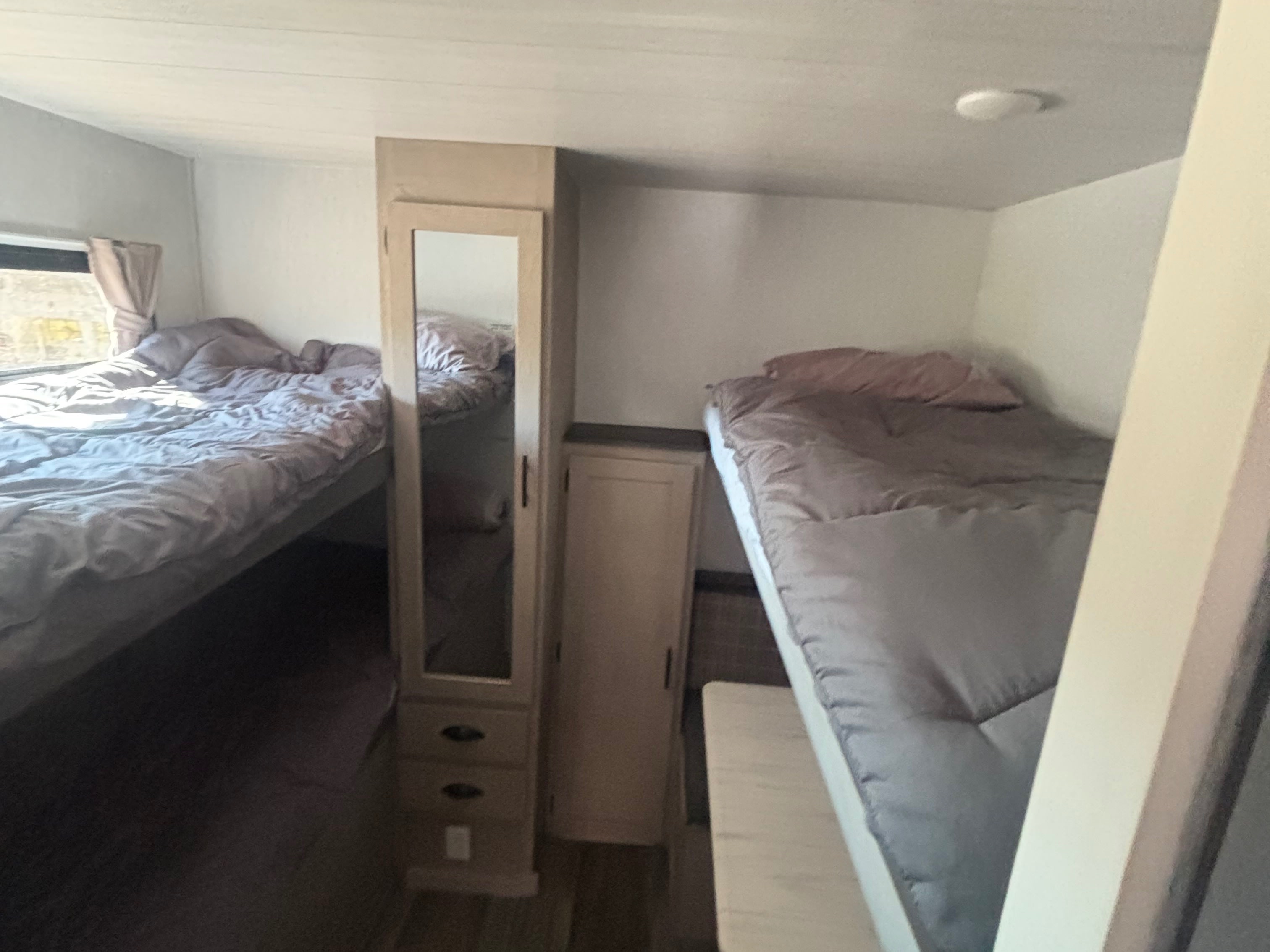 Inside this RV rental, find a comfortable bunk bed sleeping area with soft gray bedding and a central mirrored cabinet for convenience.. Forest River Evo 3005 2024