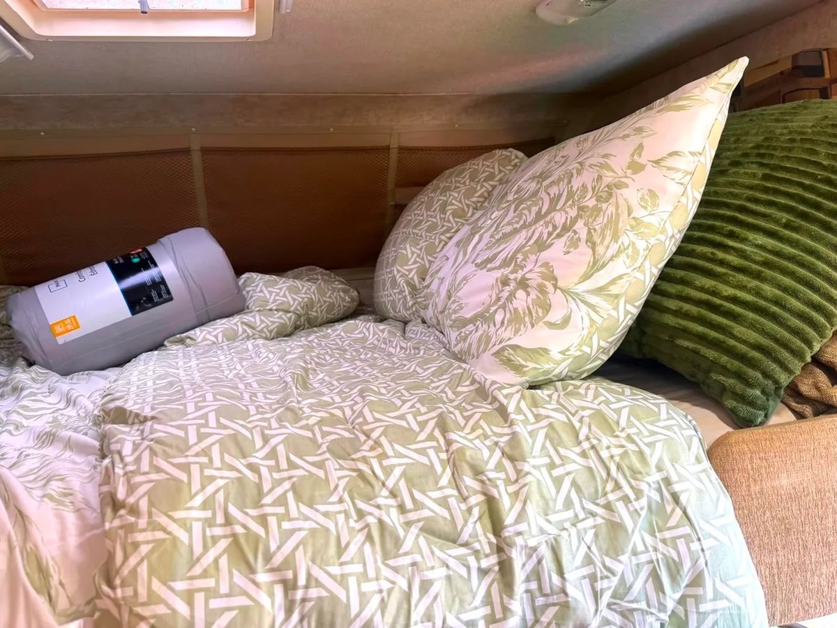 Comfortable bed in an RV rental, featuring light green bedding, floral pillows, and a rolled sleeping bag for travel comfort.. Adventurer Adventurer Motorhome 2014