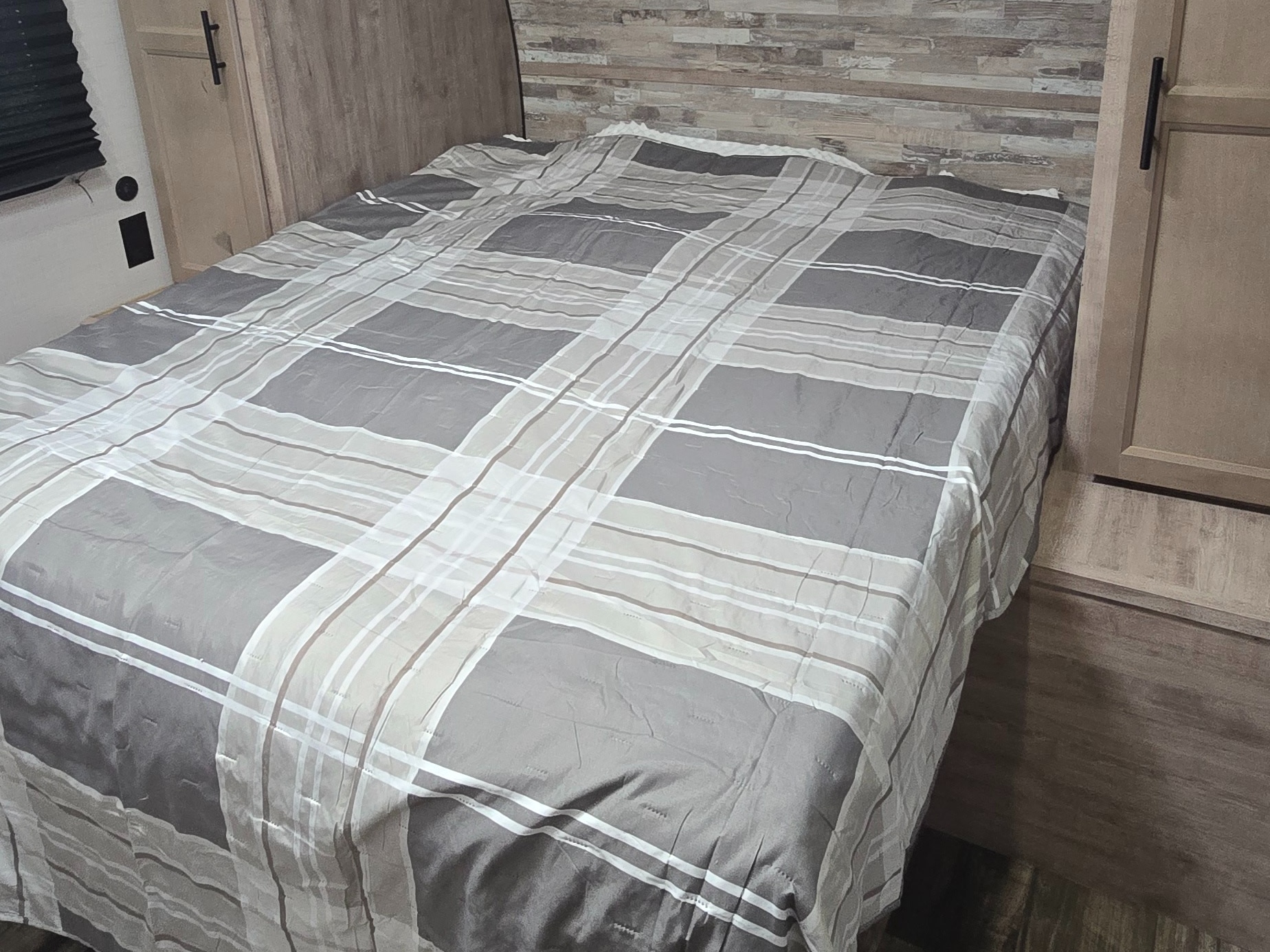 Experience comfort in this RV rental bedroom featuring a plaid comforter, compact design, and wood-paneled walls.. Gulf Stream Ameri-Lite 2024