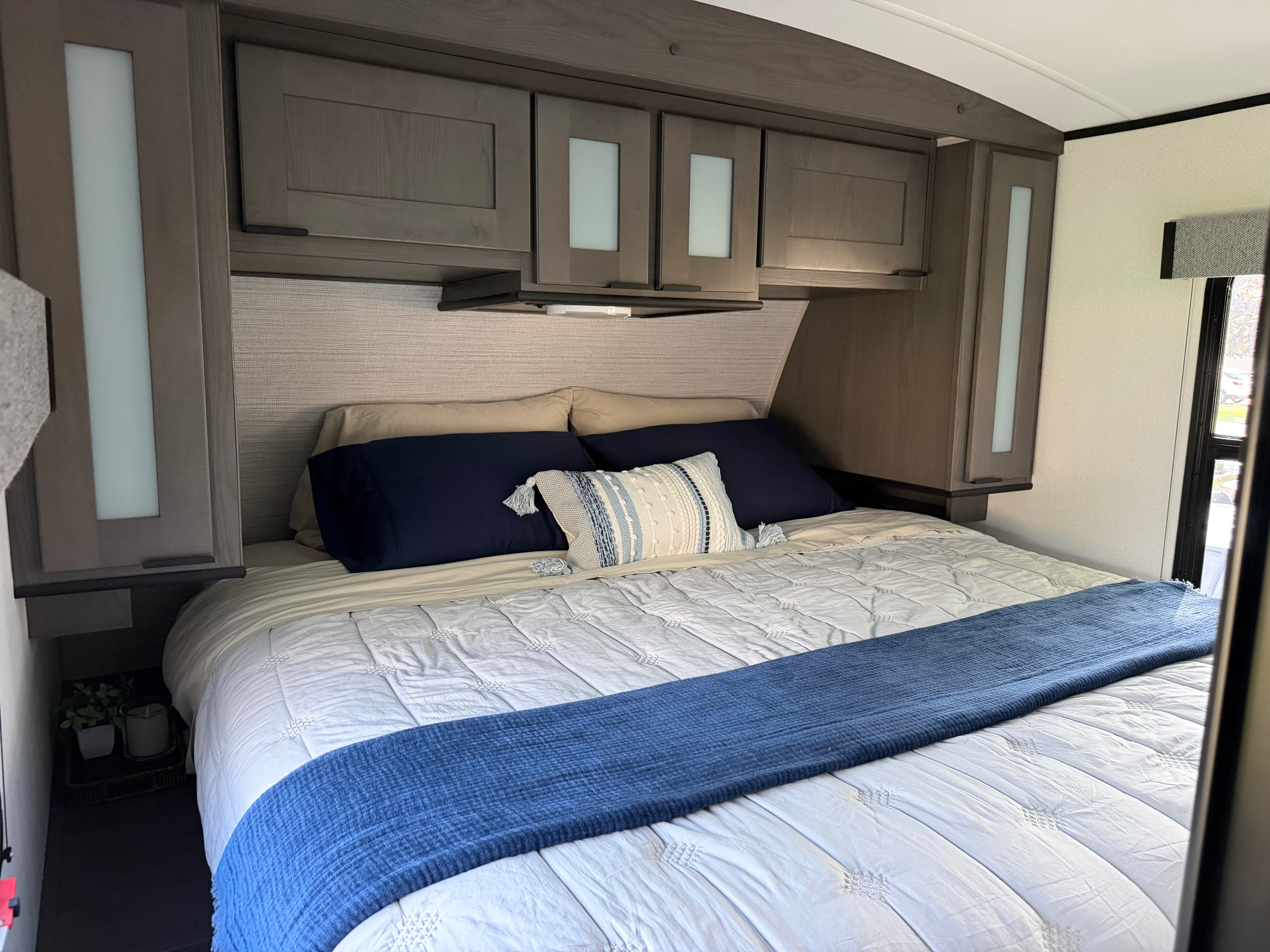 Cozy RV rental bedroom features a bed with white comforter & blue accents, plus overhead storage cabinets.. Cruiser RV MPG Ultra Lite 2022