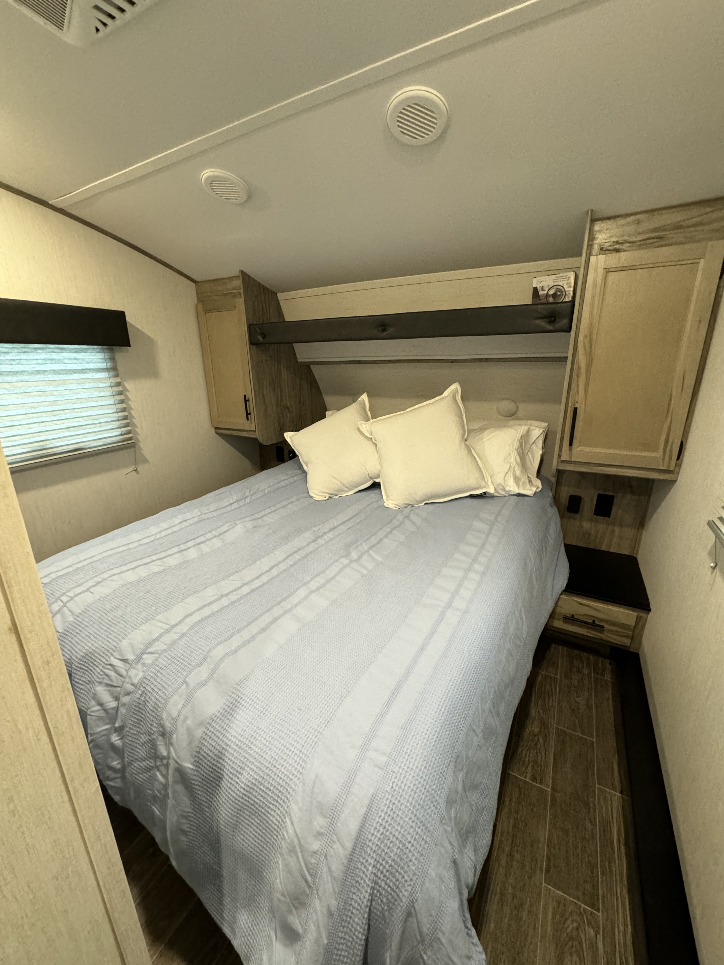 Comfortable RV rental bedroom with a bed, blue patterned comforter, nightstands, overhead storage, and window.. Forest River Cherokee Arctic Wolf 2022