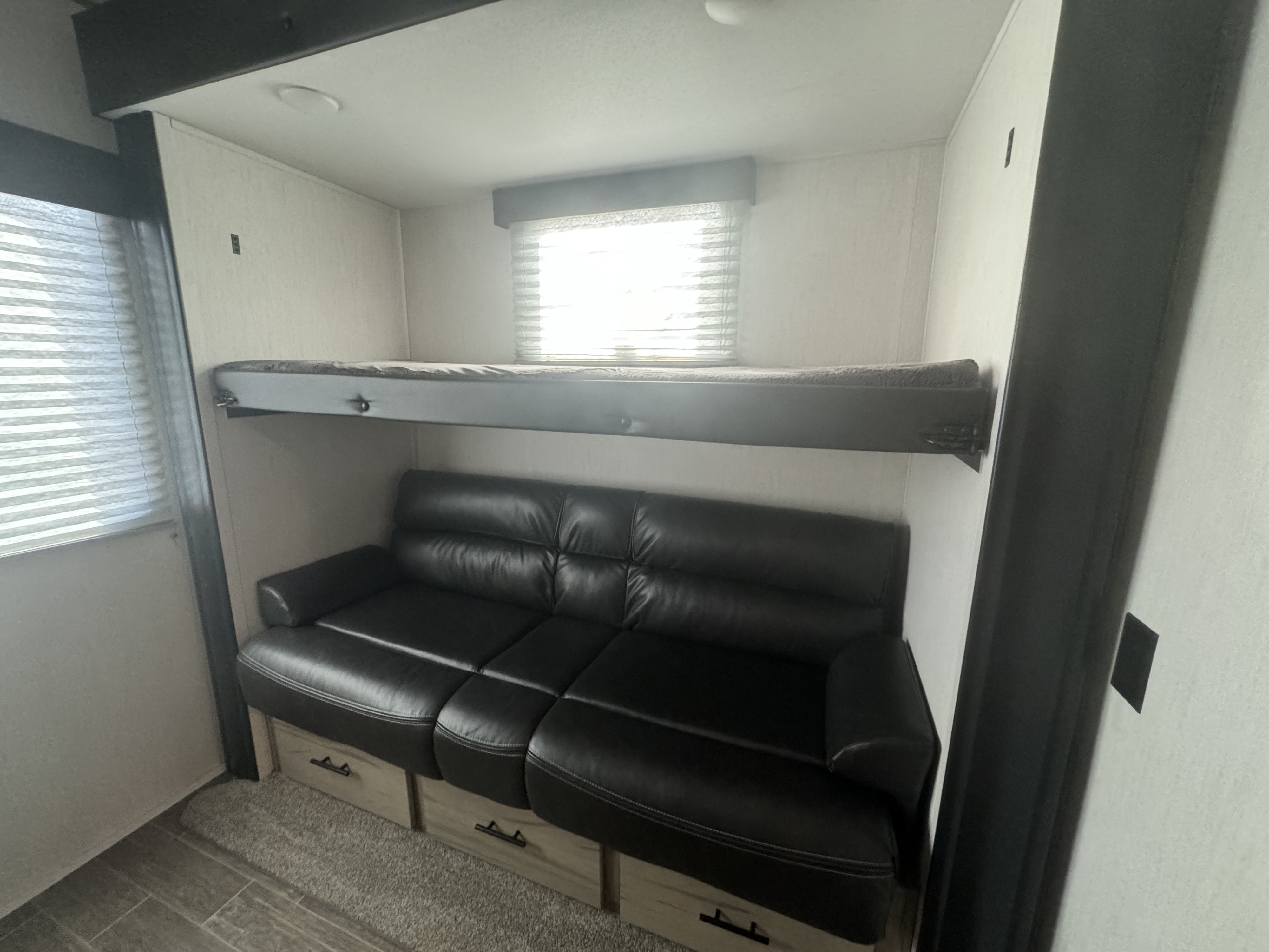 Spacious RV rental interior featuring a bunk bed above a black leather sofa with storage drawers.. Forest River Cherokee Arctic Wolf 2022