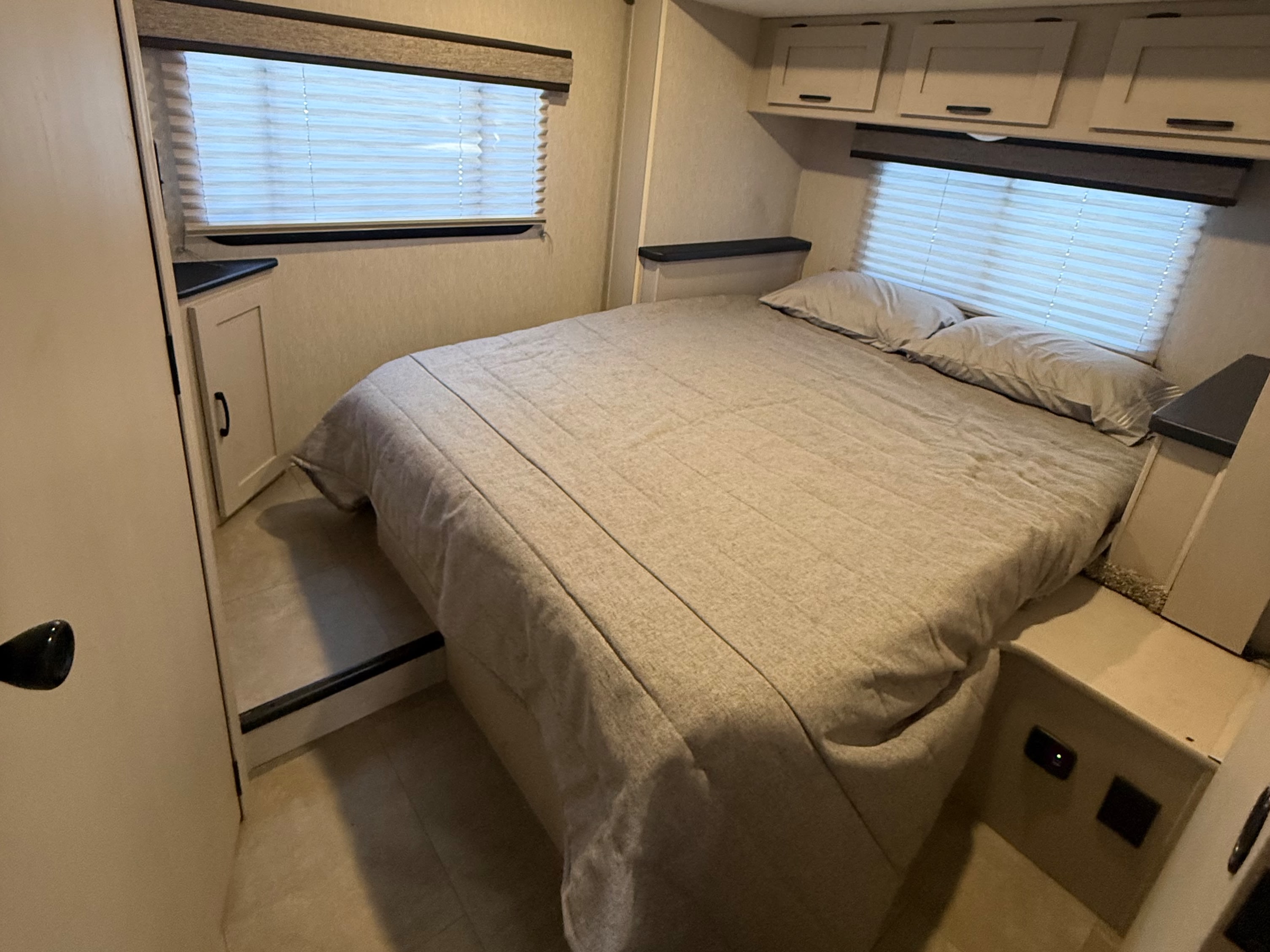 Cozy RV rental bedroom with bed, blinds, overhead cabinets, and side storage, ideal for compact living.. Forest River Coachmen Freelander 2023