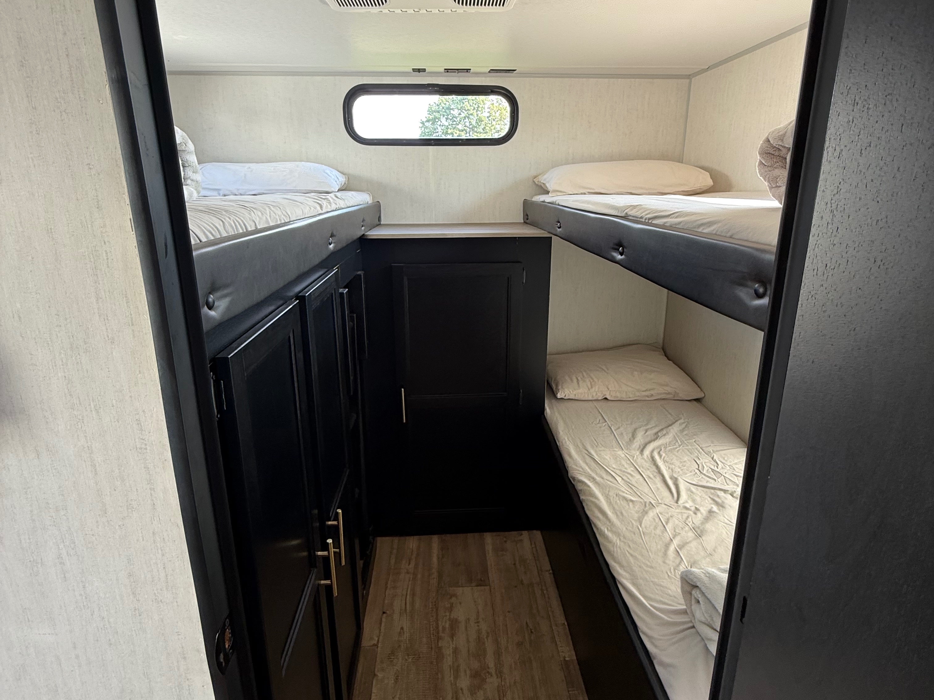 RV rental bunkhouse with four beds, including two bunk sets. Features a window, central storage, and wood-patterned floor.. Forest River Cherokee Grey Wolf 2022