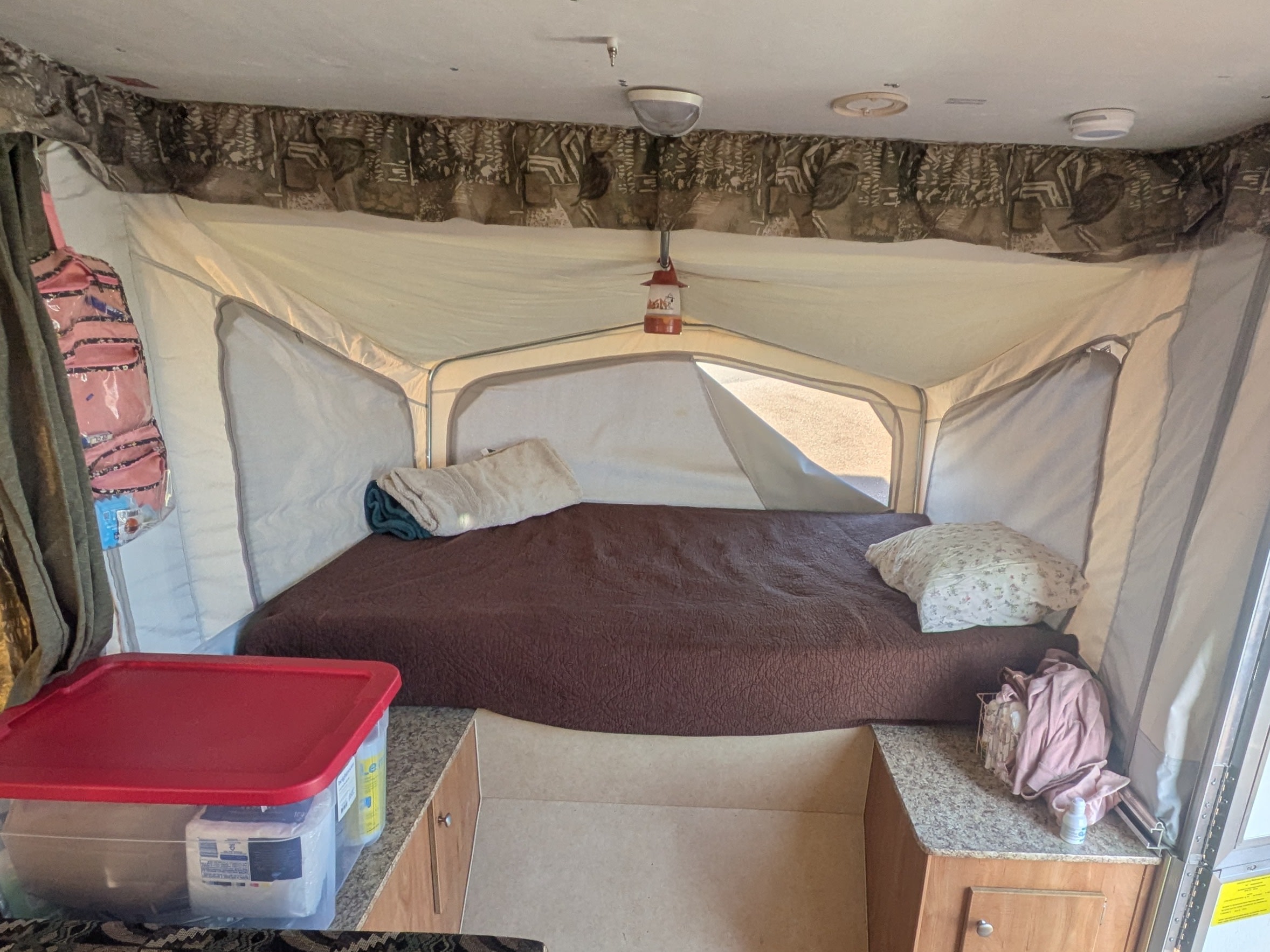 Cozy rv rental pop-up camper bed, brown comforter, white tent walls, plus clear storage bin & counter space.. Starcraft Starcraft Popup Trailer 2006