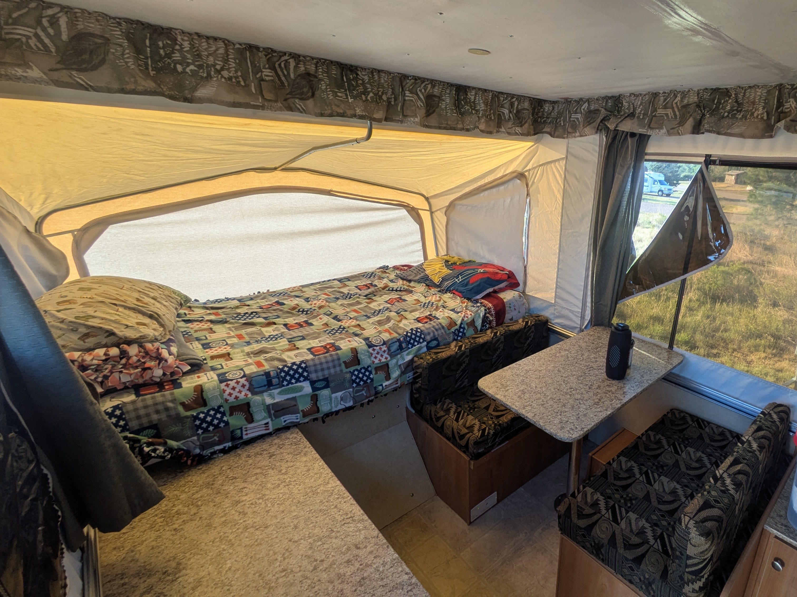 Inside an RV rental pop-up camper: bed with patchwork blanket, dinette, and bright campsite view.. Starcraft Starcraft Popup Trailer 2006