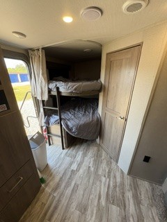 This RV rental's interior shows stacked bunk beds with a ladder, wood-look floor, and a door on the right for privacy.. Grand Design Imagine 2023