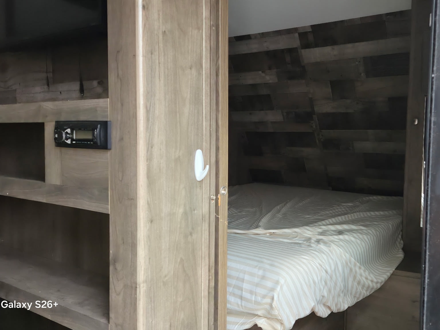 Inside an RV rental: a compact bedroom with striped bedding & wood accent wall, plus a stereo and shelving unit.. Dutchmen Aspen Trail 2020