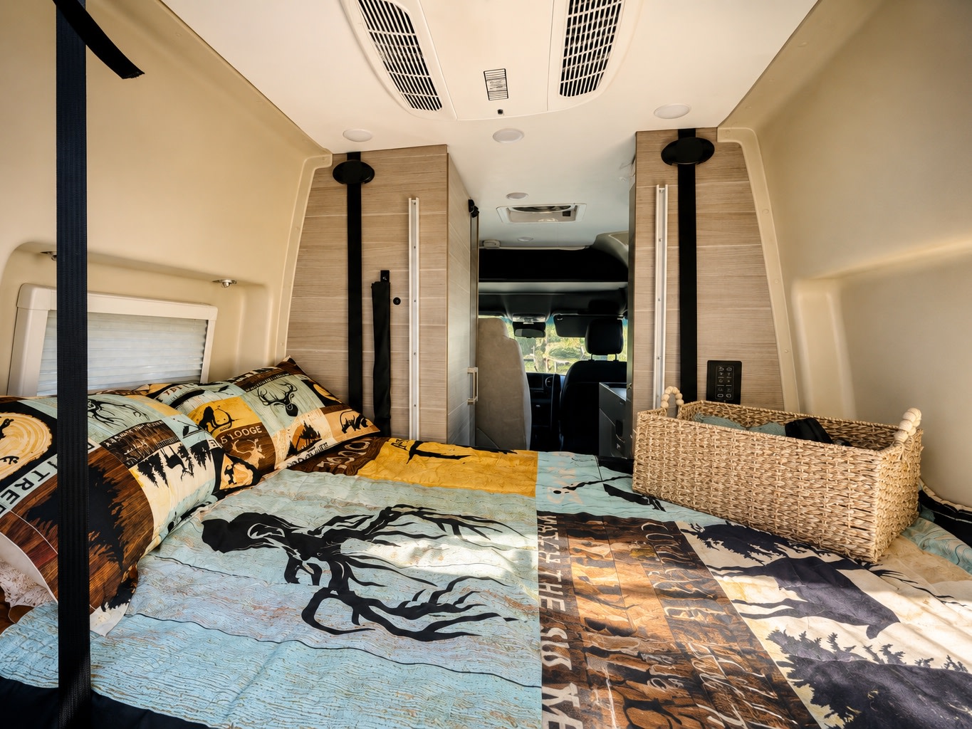 Cozy RV rental bed with nature-themed bedding, overhead AC, and front cab view. Perfect for travel adventures.. Entegra Coach Launch 2024