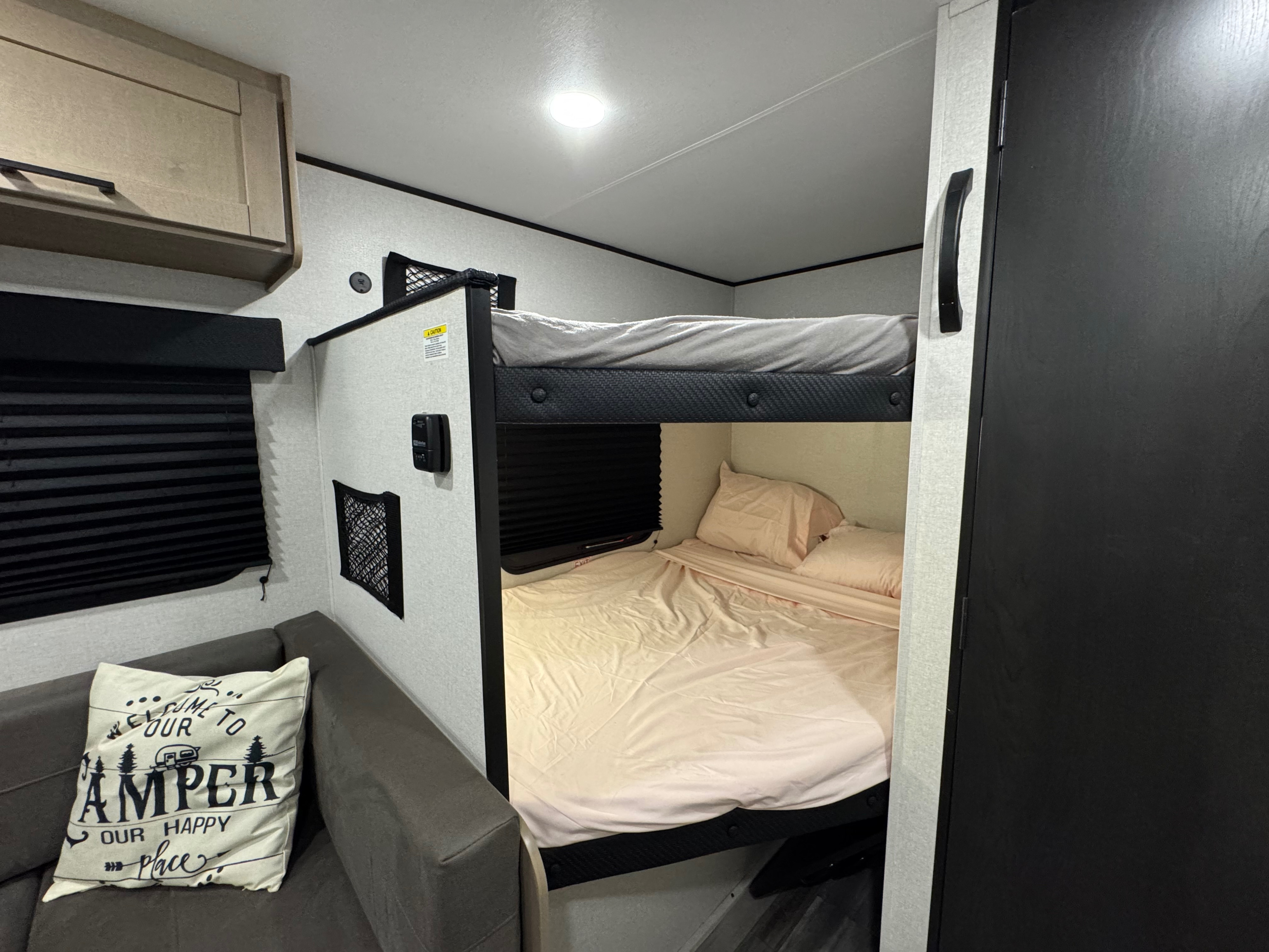 Inside an RV rental: two stacked bunk beds with light bedding, a grey sofa with a 'Camper' pillow, and a window with blinds.. Jayco Jay Flight SLX Sport Edition 2026