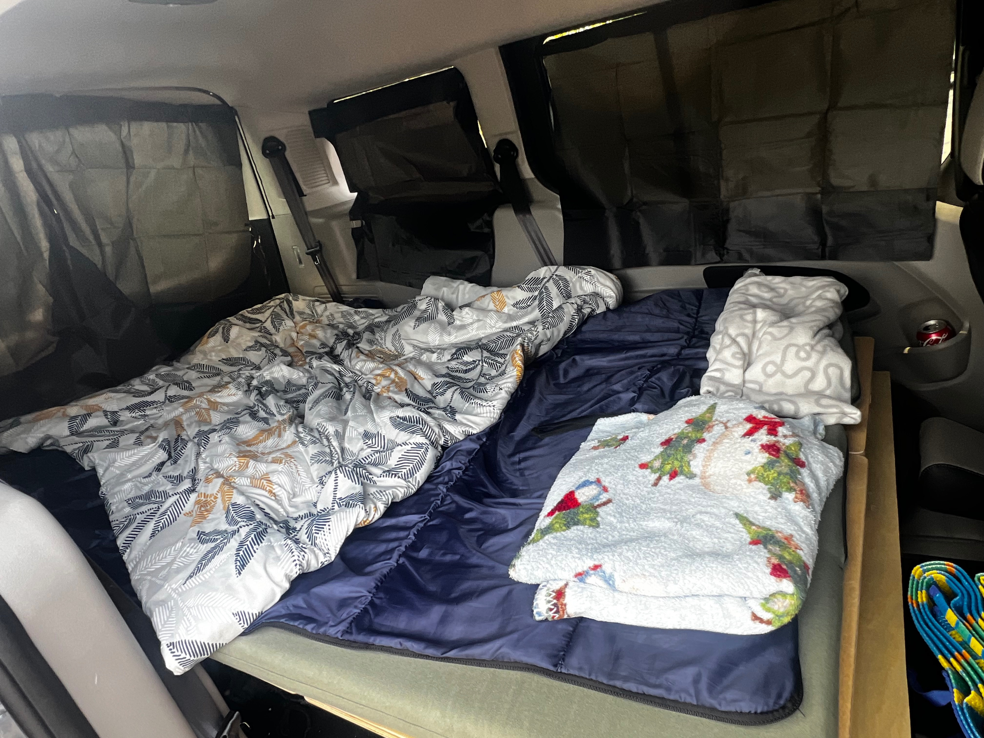 Cozy RV rental interior: a bed made with patterned and festive blankets, dark window covers, and a can in a cup holder.. Ford transit 2019