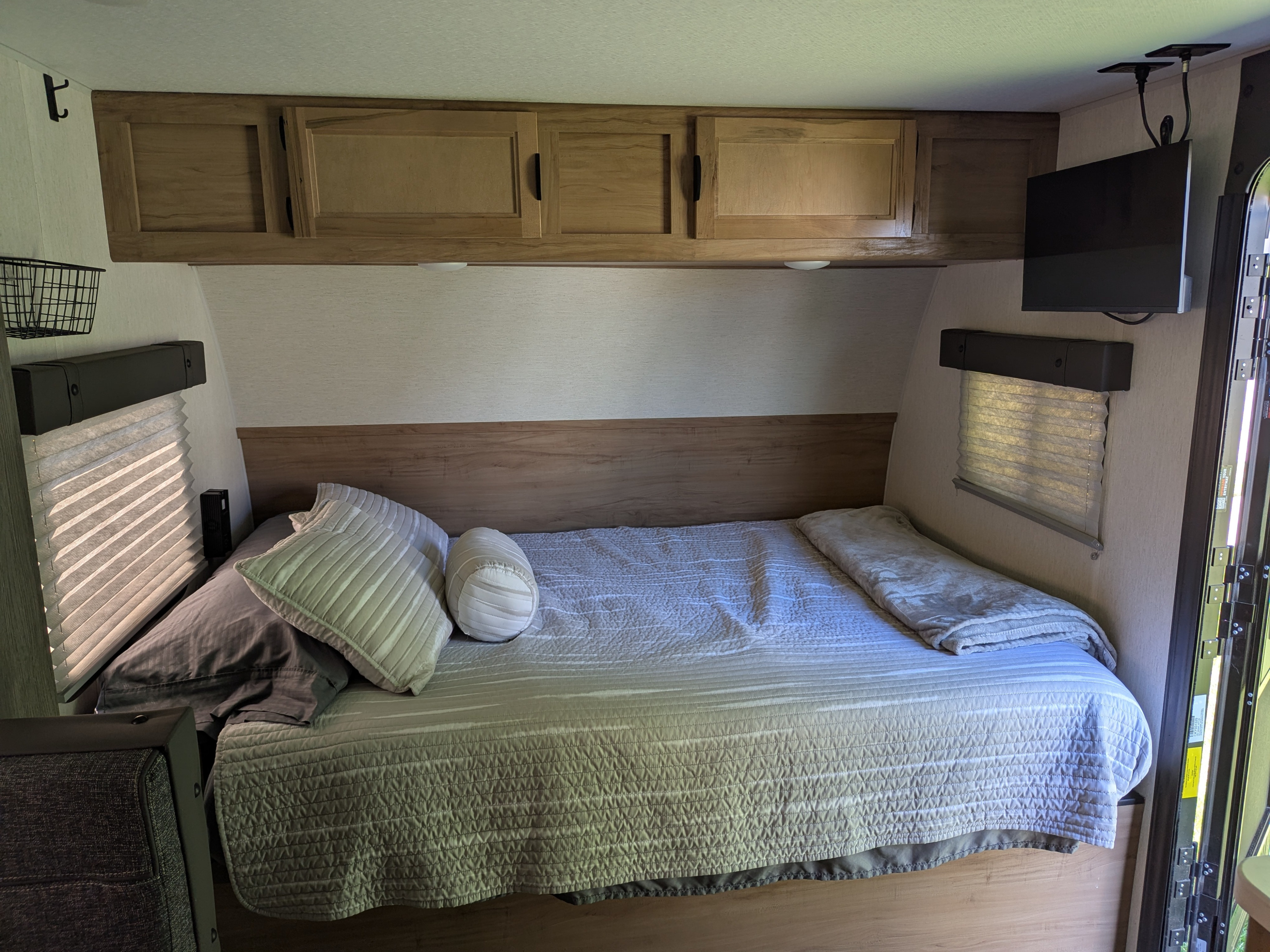 Inside an RV rental: a compact bedroom with a cozy bed, light wood cabinets, TV, and window blinds for comfortable travel.. Forest River Cherokee Wolf Pup 2024