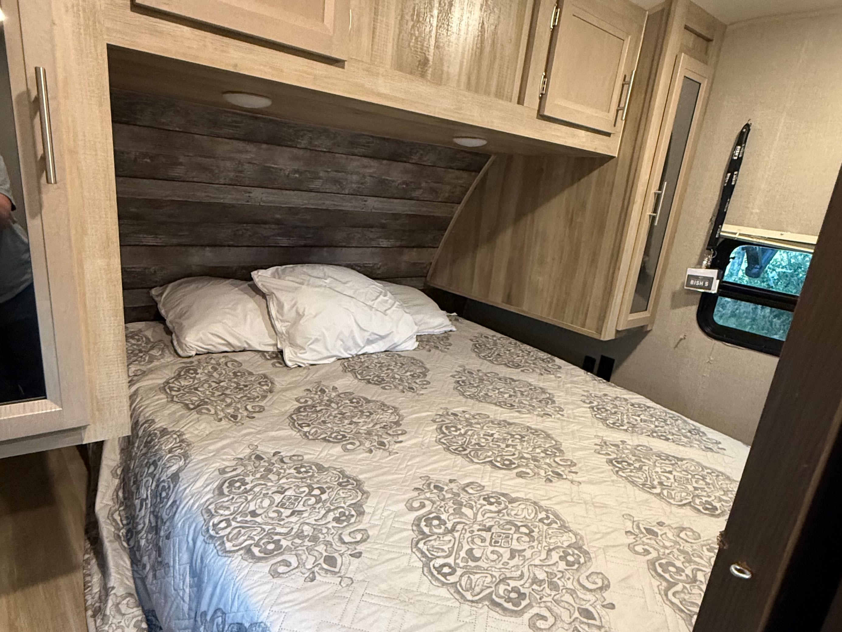 Inside an RV rental: a compact bedroom featuring a comfortable bed, wooden headboard, and overhead storage.. Coachmen Catalina Trail Blazer 29 THS Toy Hauler 2021