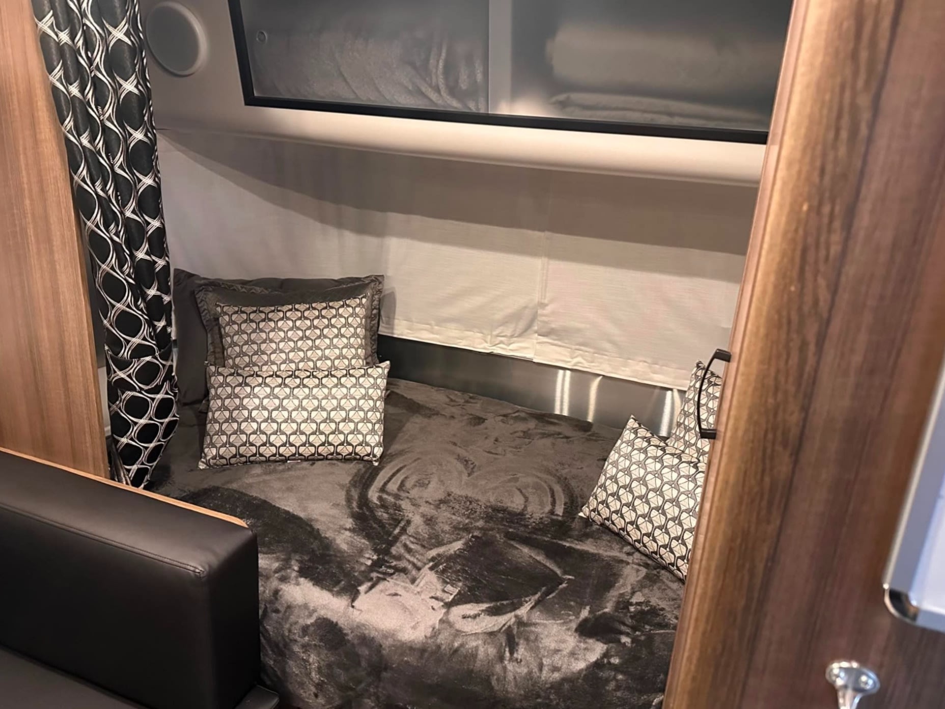 Cozy RV rental bedroom featuring a bed with patterned pillows, a dark blanket, and an elegant patterned curtain.. Airstream Caravel 2023